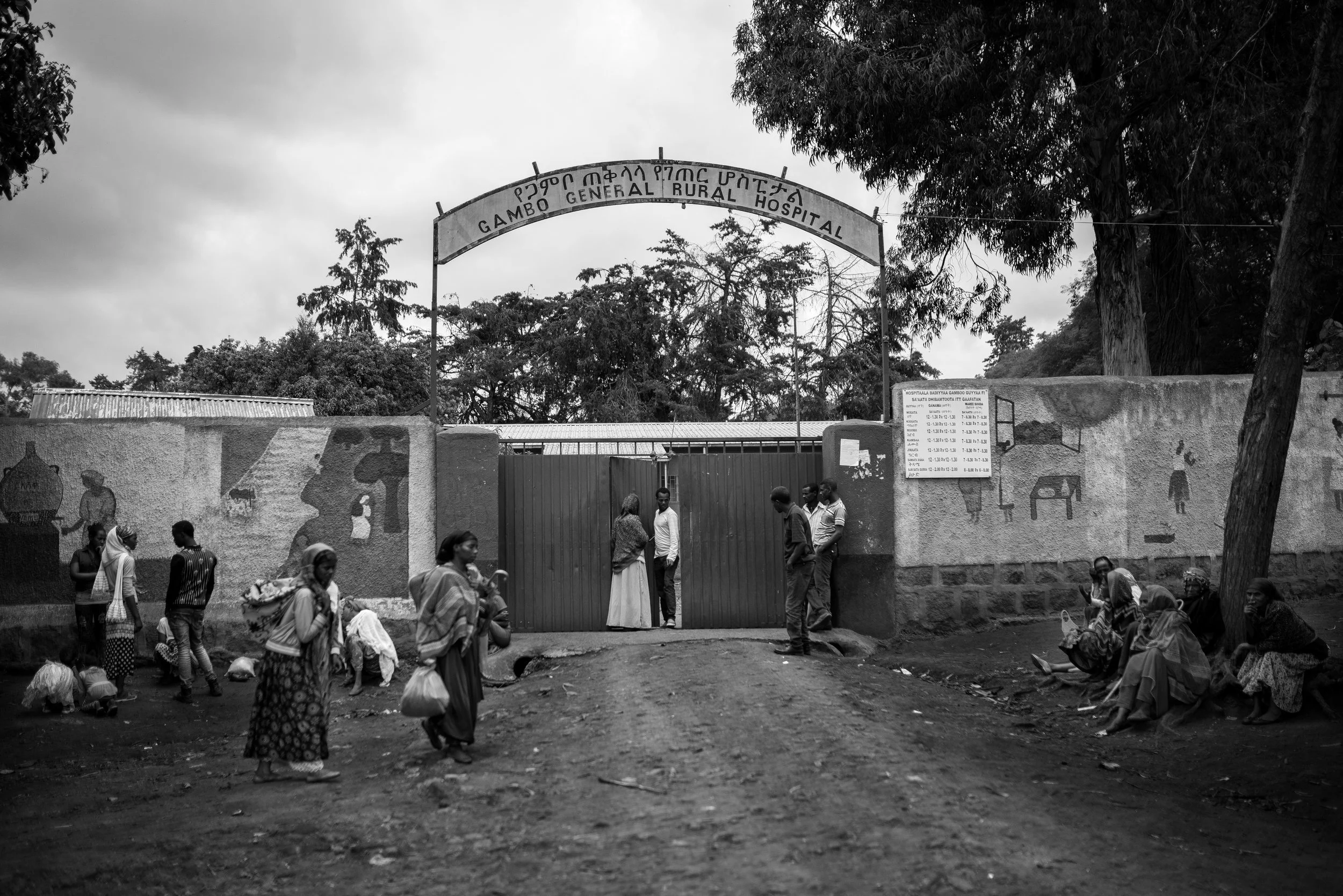 Entrada al hospital general rural Gambo, con varias personas esperando afuera y un cartel informativo.