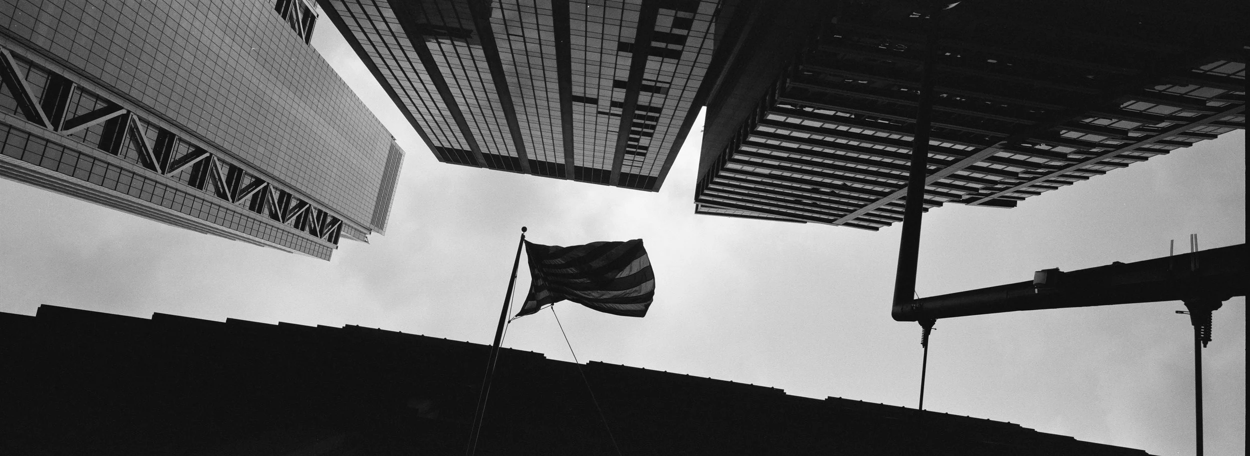 Vista de edificios altos en la ciudad con una bandera estadounidense ondeando en primer plano, en un cielo nublado y oscuro.