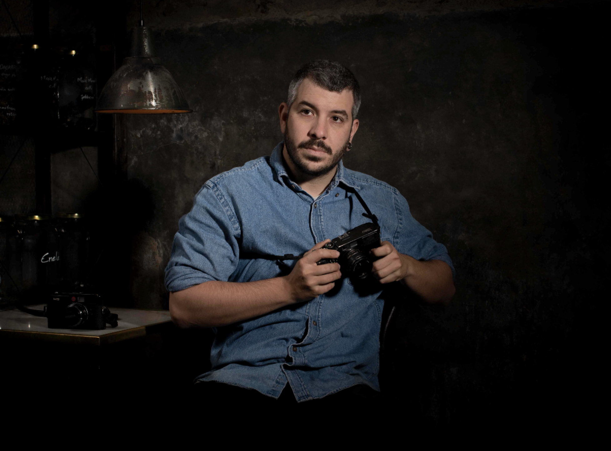 Hombre con barba y cabello corto, sosteniendo una cámara en un ambiente oscuro