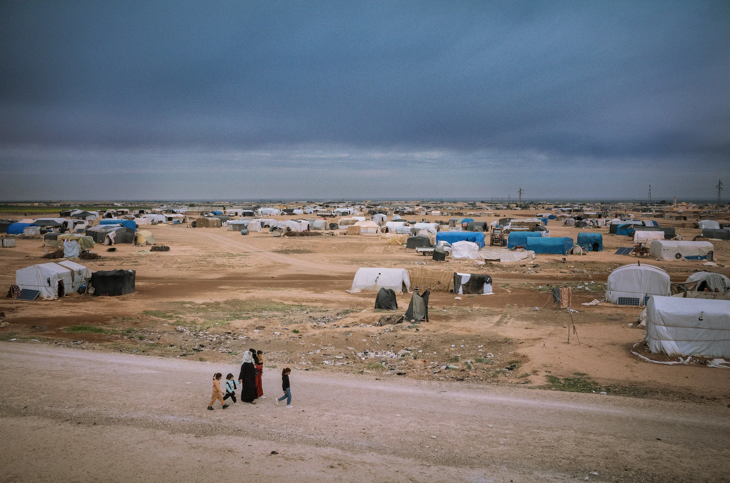 Un campamento de refugiados con muchas tiendas de lona y personas caminando en primer plano