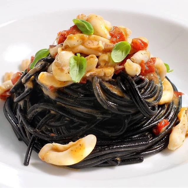 Black pasta topped with baby calamary and garnished with basil leaves on a white plate