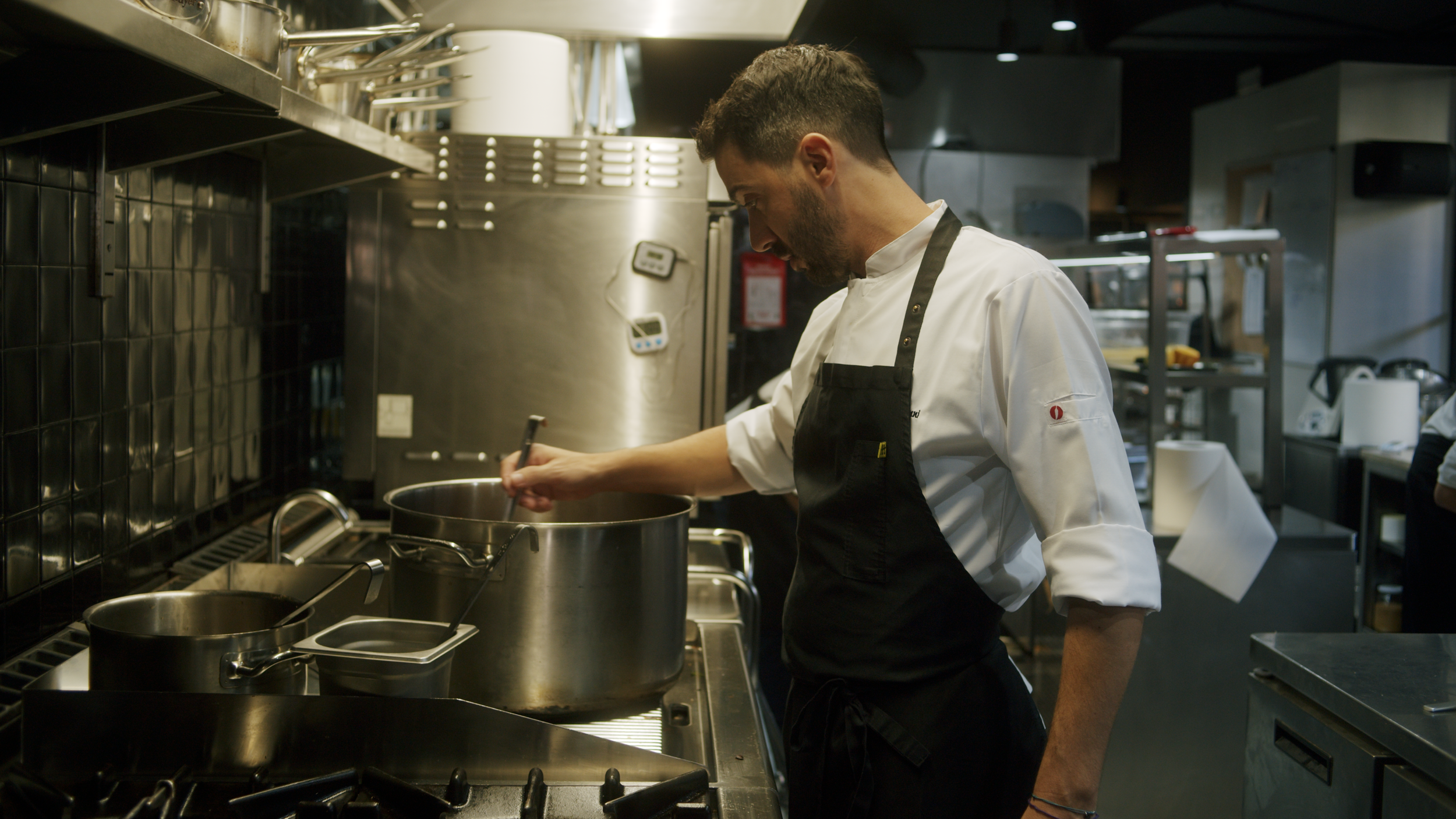 Chef stirring a large pot in a professional kitchen.