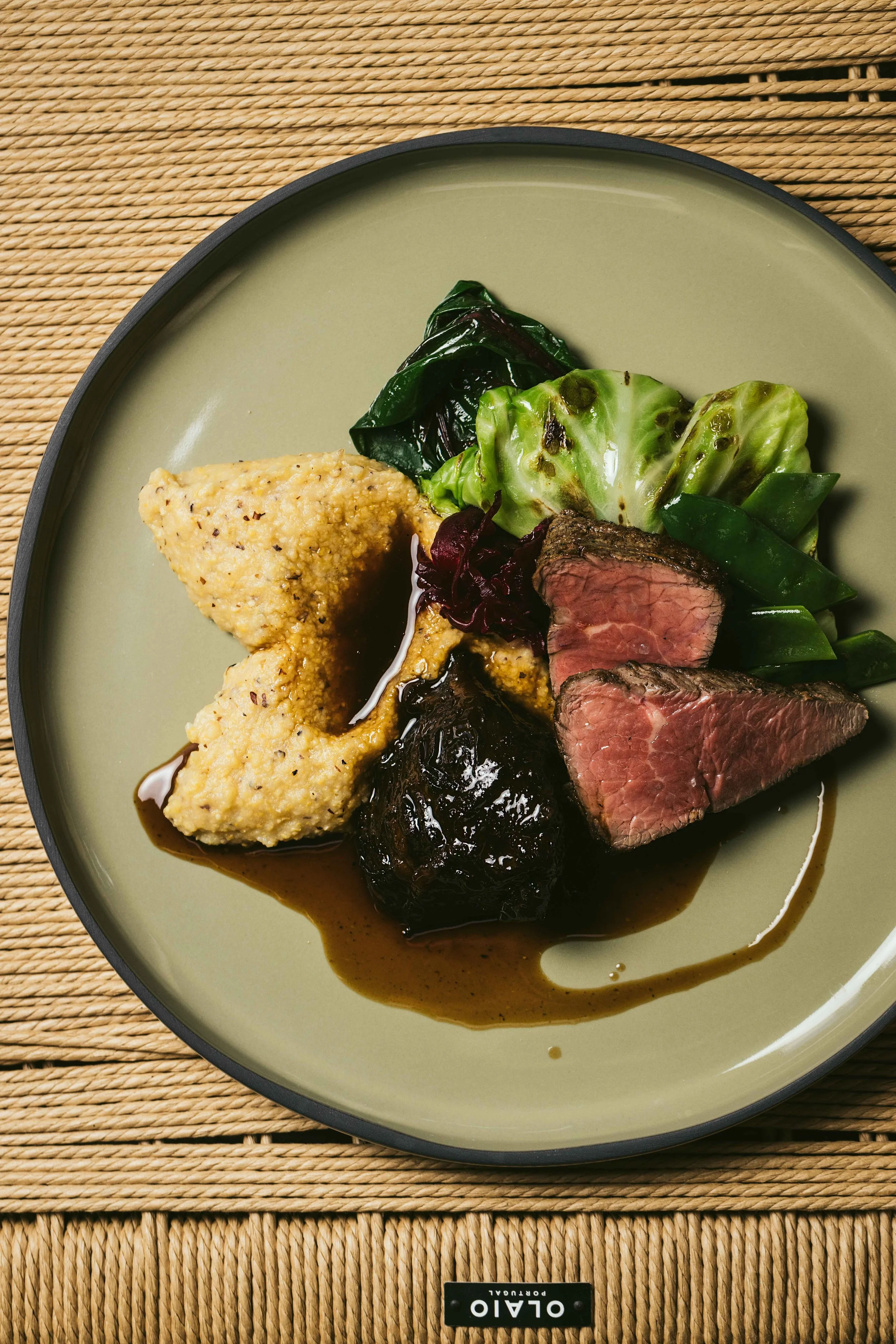 Plate with portions of cooked steak, fried chicken and vegetables including leafy greens, green beans, and lettuce, all drizzled with sauce.