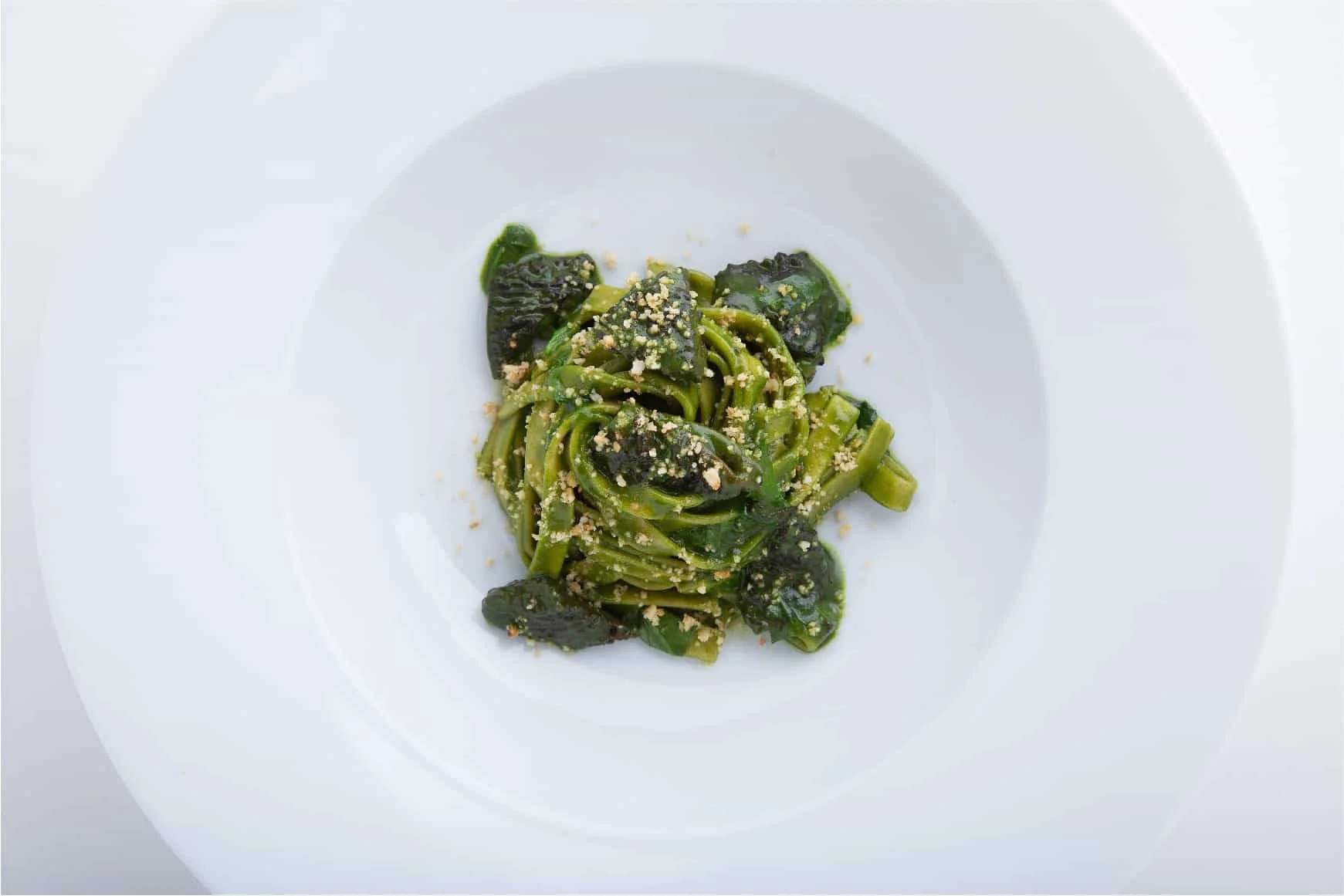 Plate of green pasta with leafy greens and sprinkled with grated hazelnuts.