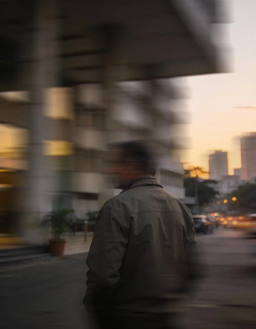 A male business owner stands on a street in India as life flashes past him. This image represents the stresses and the noise that business owners face.