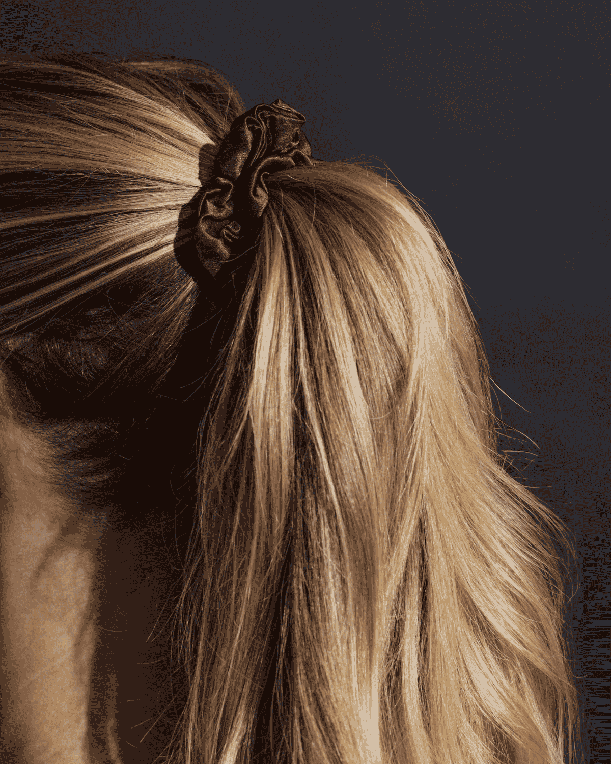 Refined Mane chocolate silk scrunchie securing blonde hair in a ponytail.