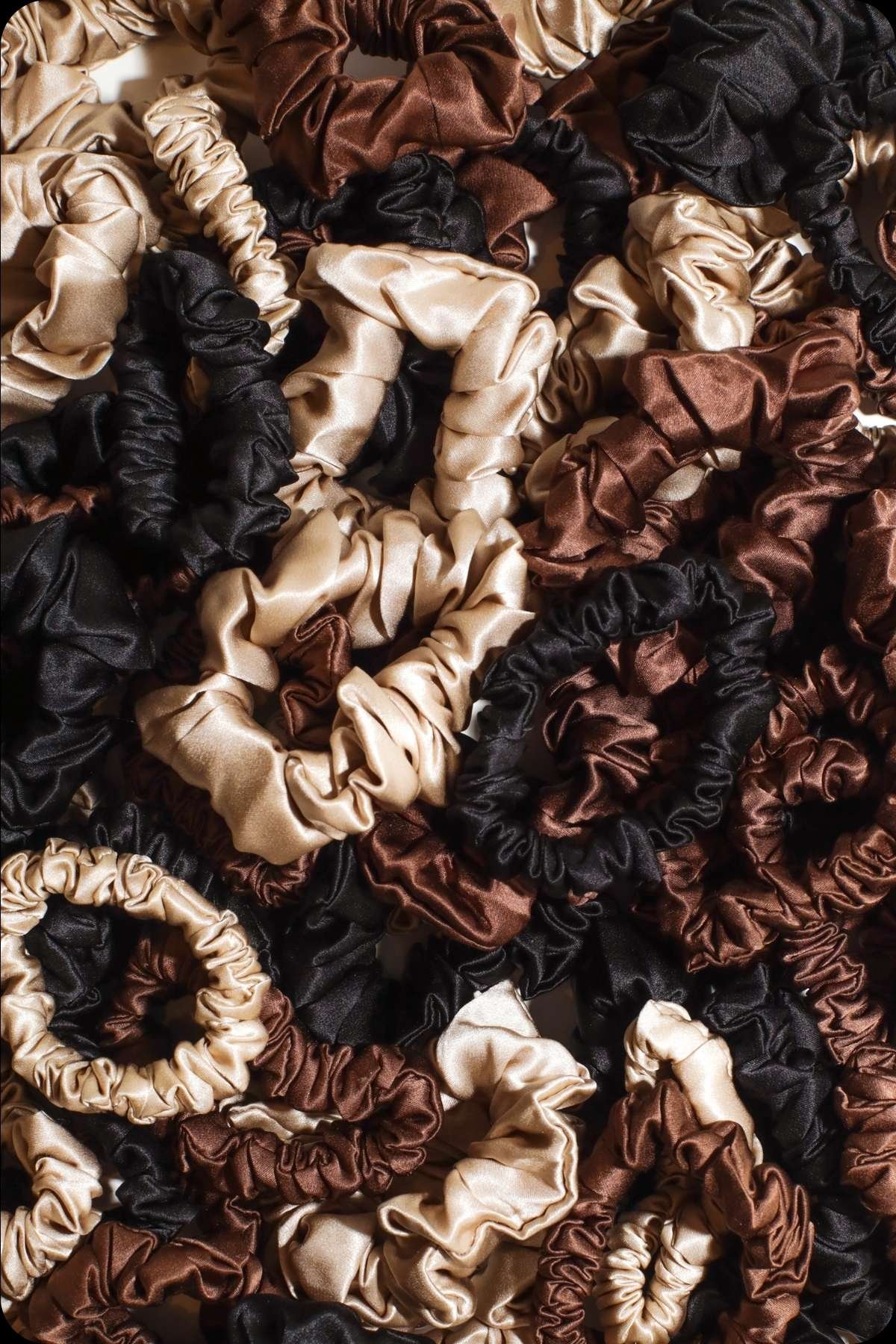Close-up flat lay of Refined Mane silk scrunchies in champagne, chocolate, and onyx.
