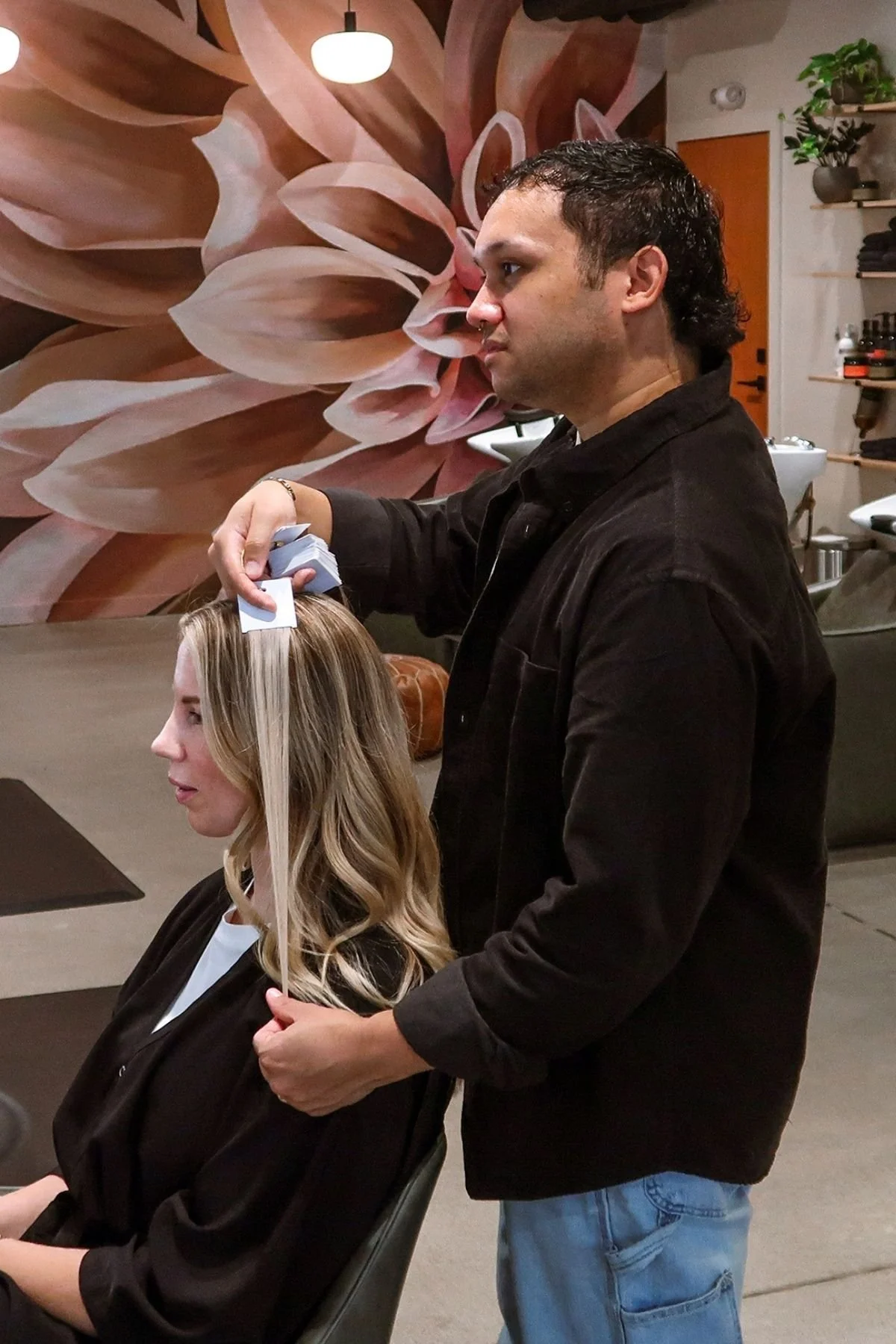 Hairstylist and founder of Refined Mane Chad Creasey working with a client installing hair extensions.