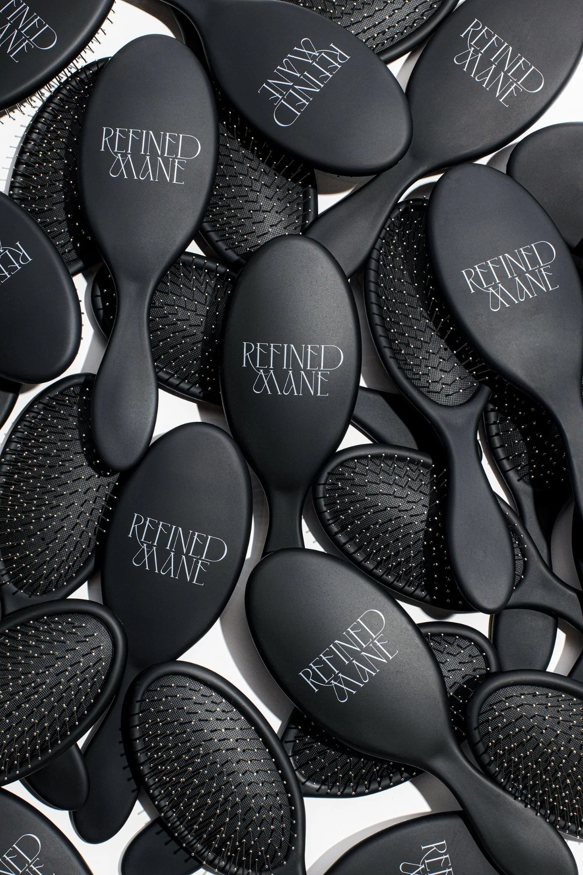 Flat lay of matte black Refined Mane hair brushes arranged on a white background.