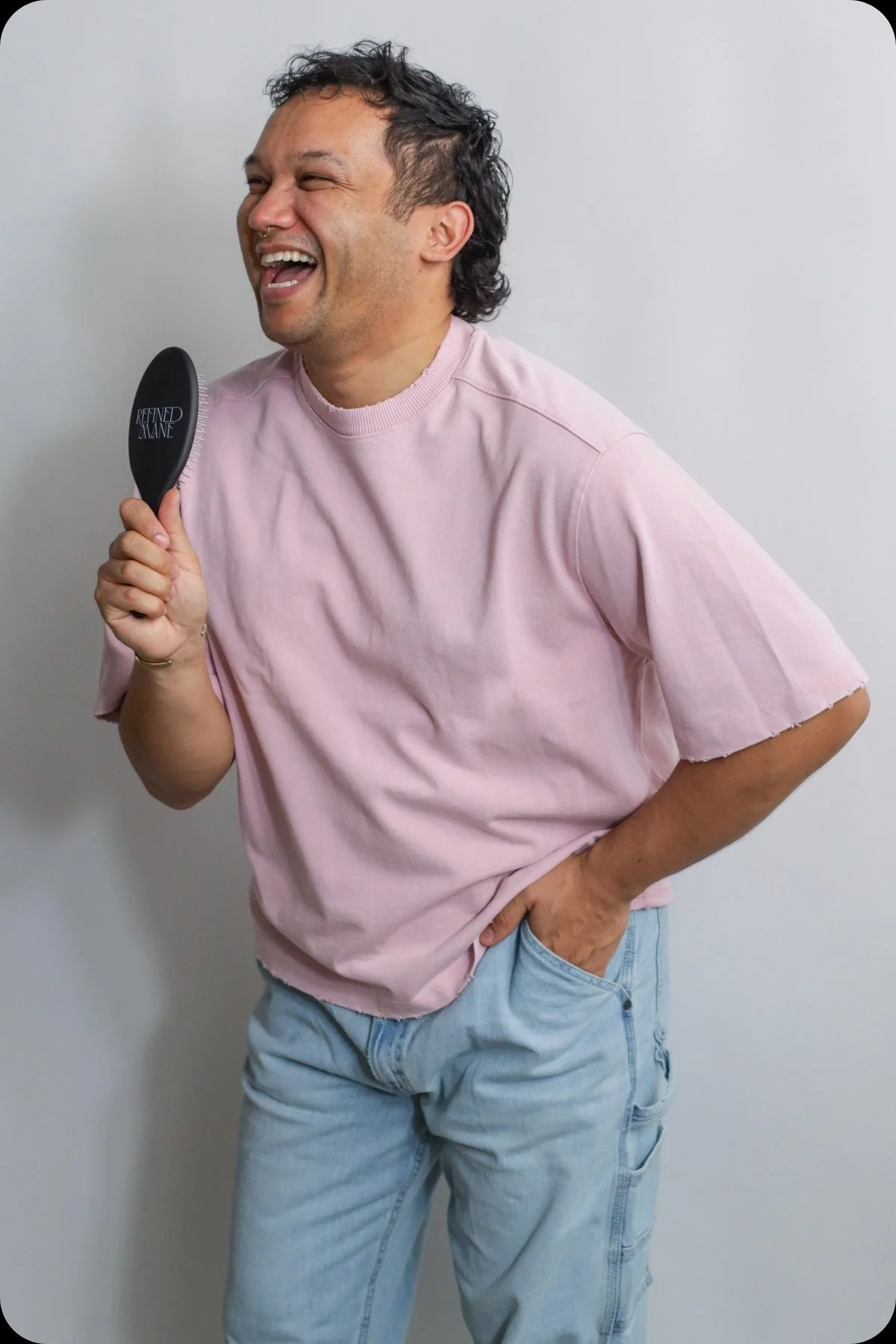 Chad Creasey, founder of Refined Mane, smiling while holding a black Refined Mane hair brush against a white wall.