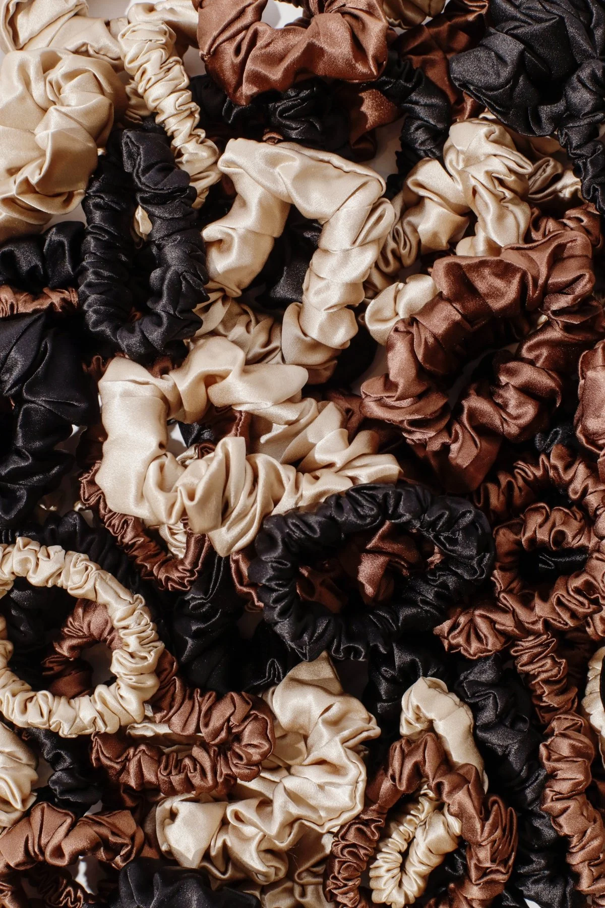 Flat lay of Refined Mane silk scrunchies in champagne, chocolate, and onyx colors.