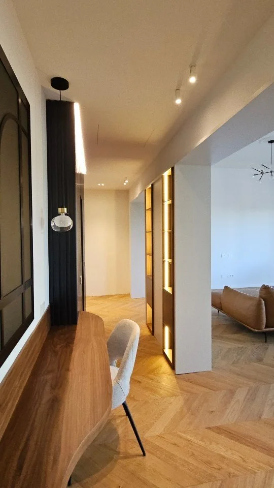Interni moderni di un appartamento con scrivania in legno, sedia beige, pareti bianche, lampade da soffitto e arredi in stile minimalista.