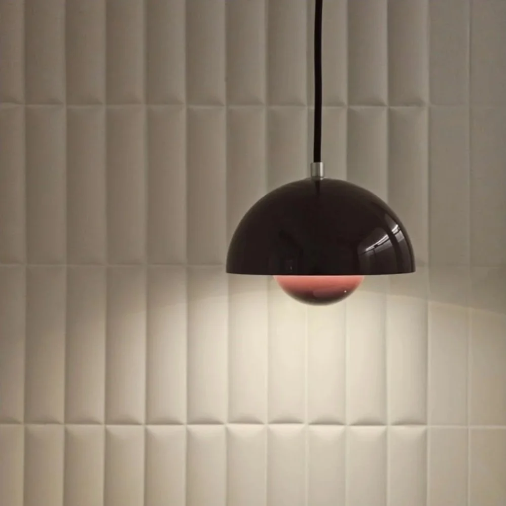Lampada sospesa di colore nero con riflessi, illuminata in una stanza con pareti rivestite di pannelli imbottiti beige.