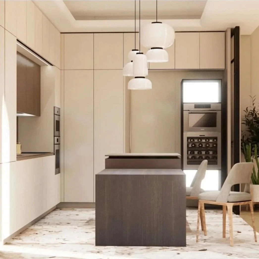 Interno cucina moderna con isola centrale, armadi chiari, luci pendenti bianche e pareti beige, finestra con elettrodomestici integrati, tavolo con sedie chiare e piante decorative.