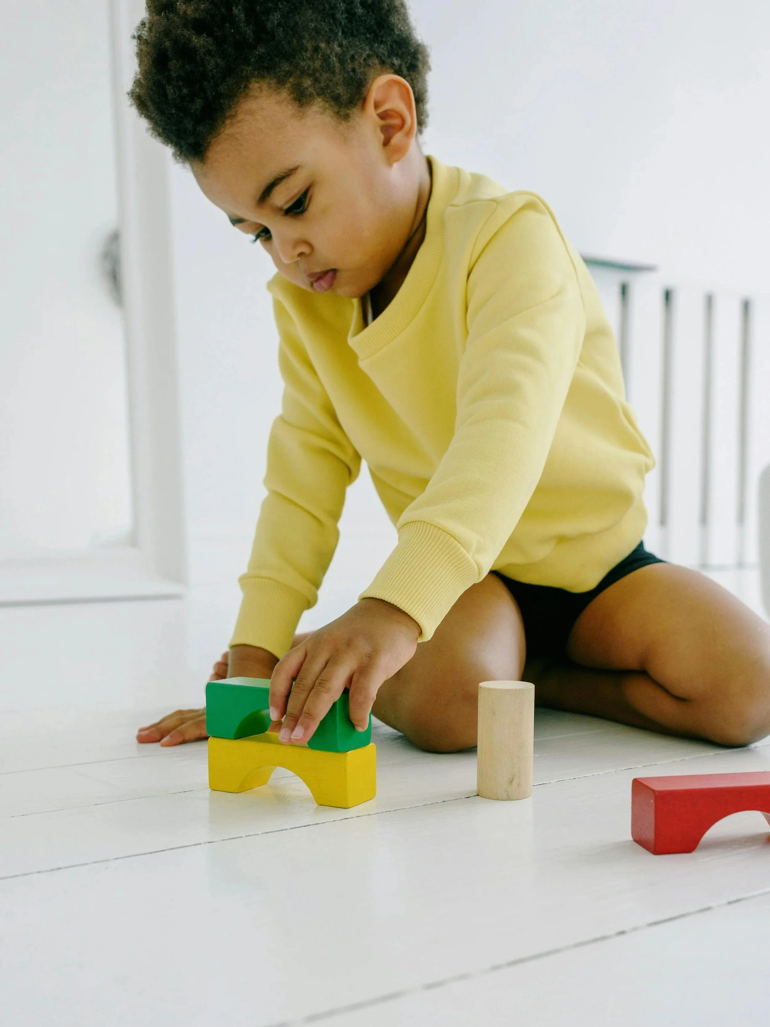 A young child playing with colorful wooden blocks on a white floor indoors.