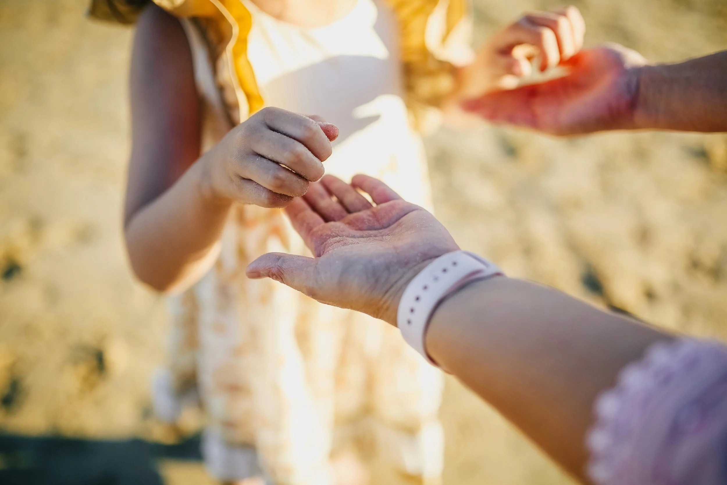 Child and adult holding hands, outdoors in sunny weather.