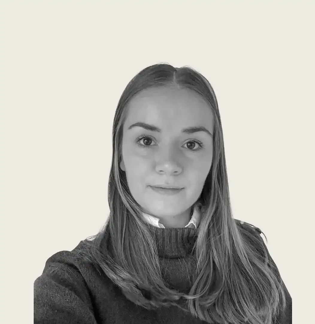 Portrait en noir et blanc d'une jeune femme avec de longs cheveux, portant un pull et une chemise, souriant légèrement, devant un fond clair.