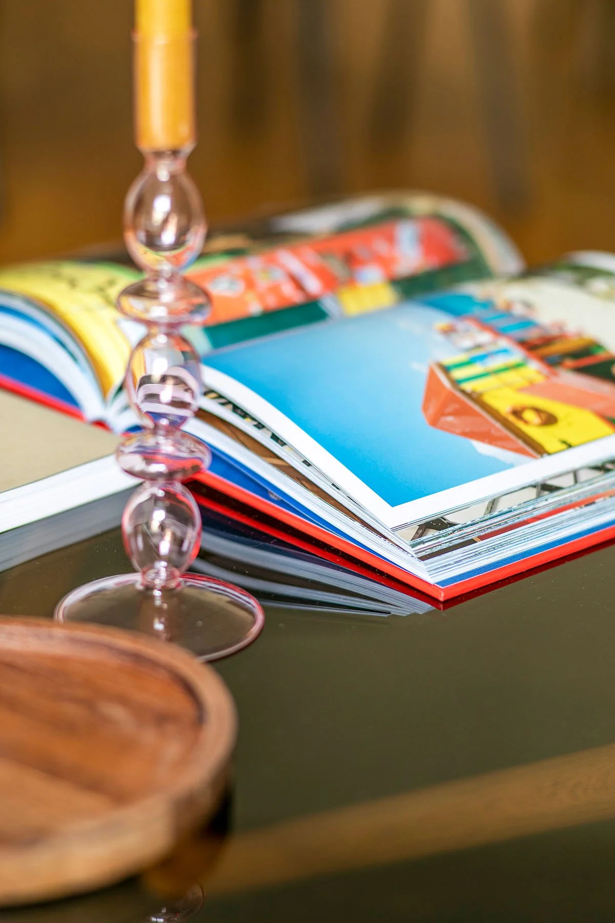 Un livre ou un magazine ouvert avec des pages colorées, posé sur une table noire, avec un verre à pied en verre transparent à côté.