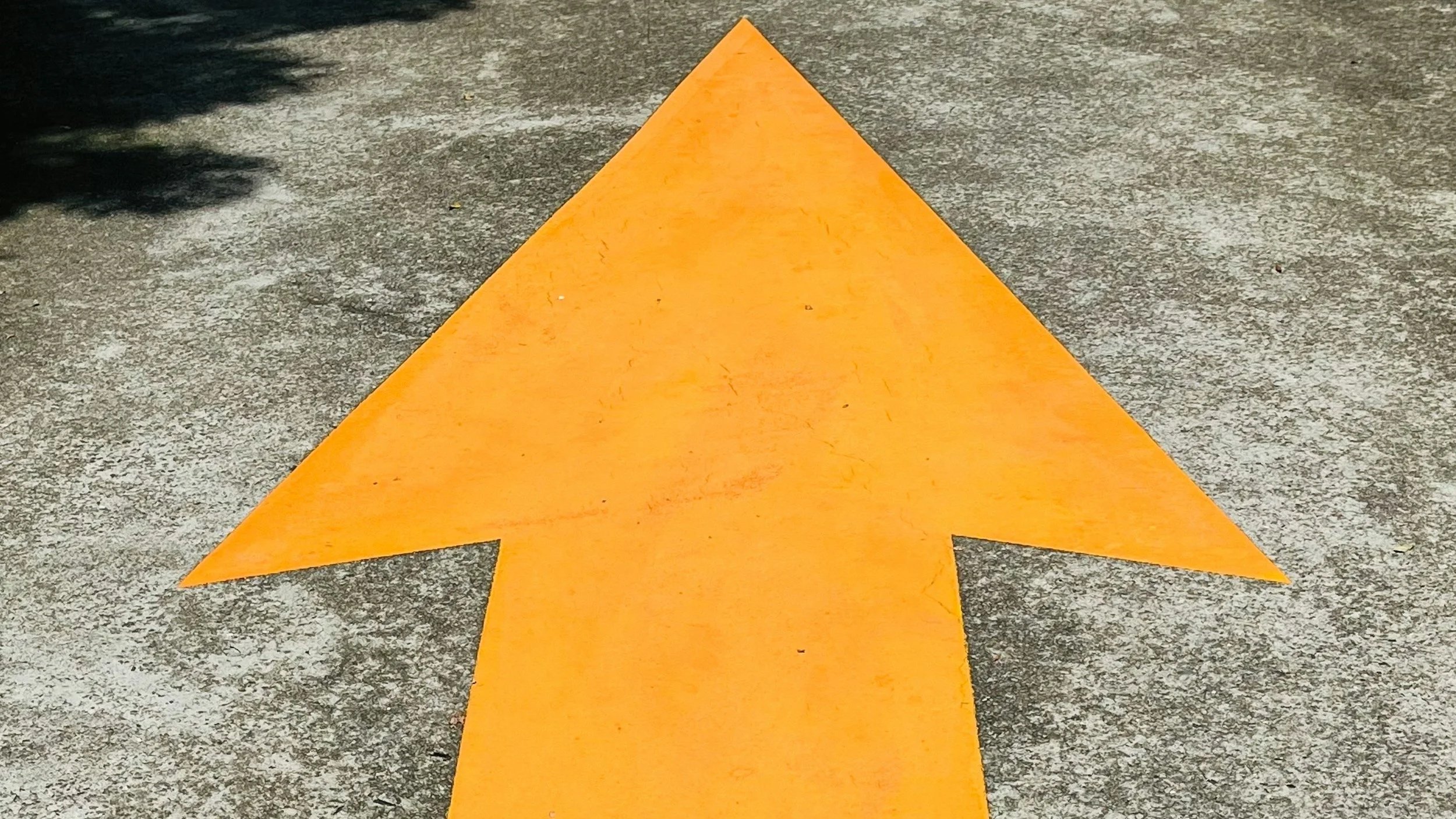 Gelbe Richtungspfeil auf asphaltierter Straße, zeigt nach vorne.