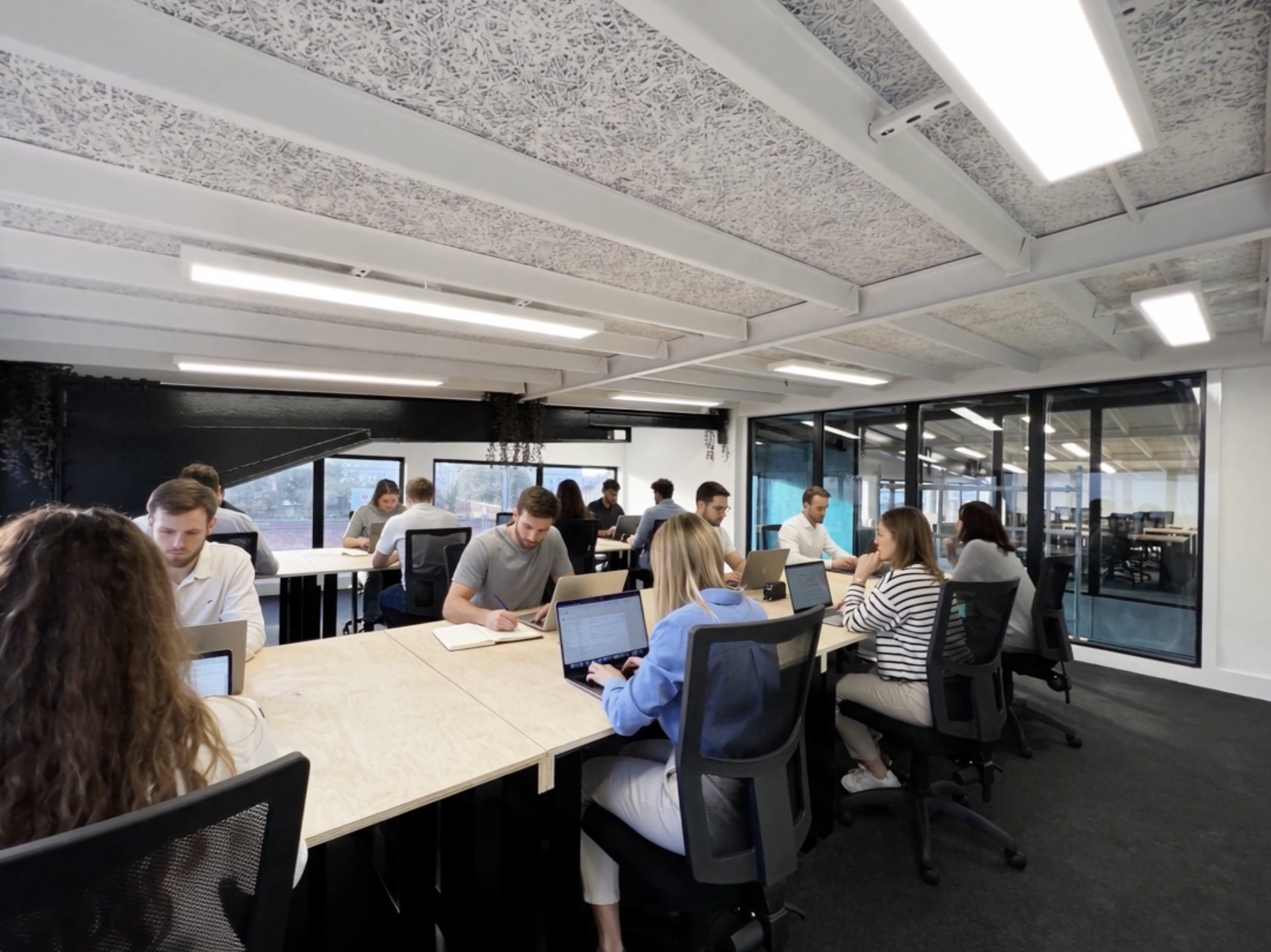 People working on laptops in a modern conference room with large windows and ceiling lights.