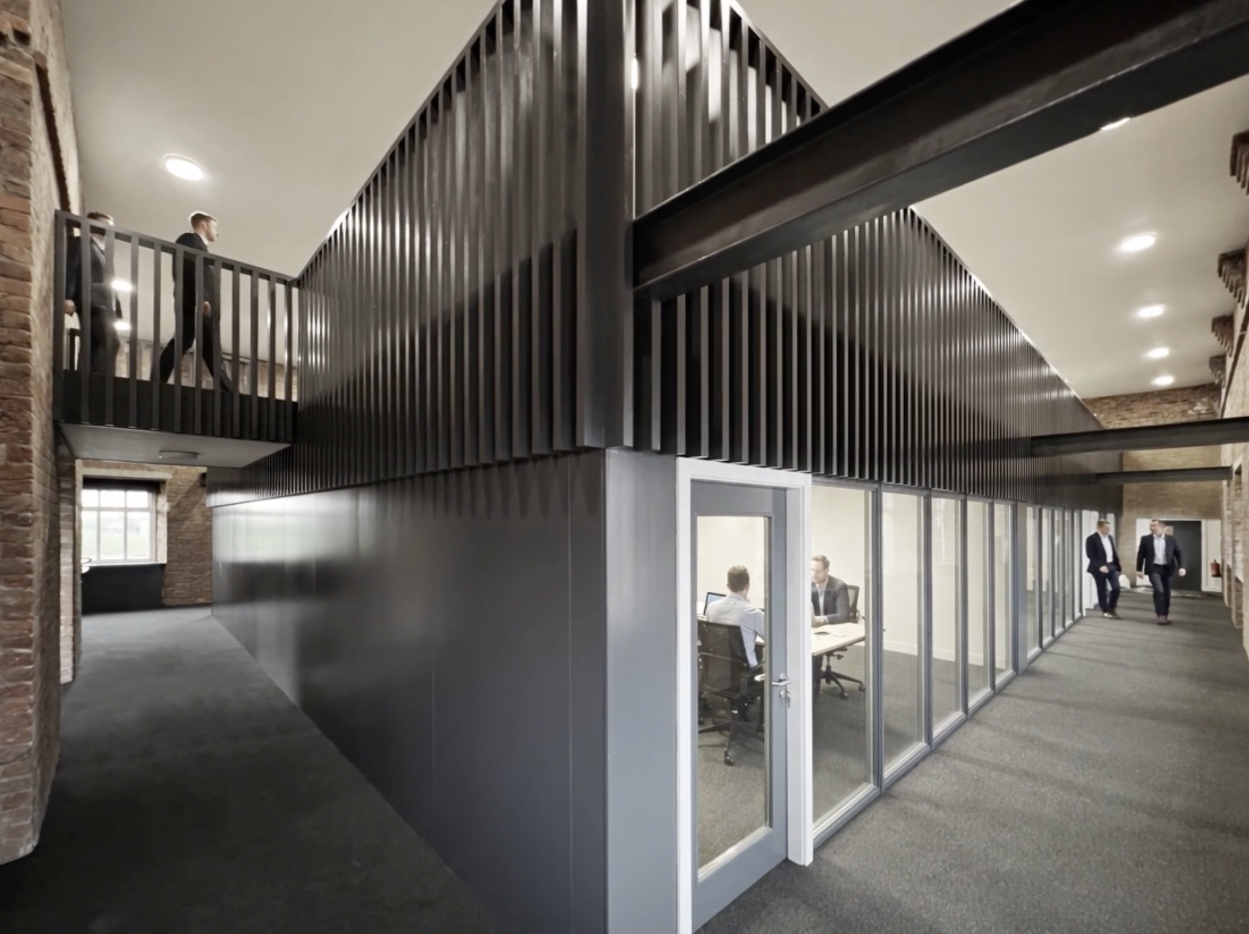 Business professionals walking through an office space with a modern black metal railing and glass-walled conference rooms.