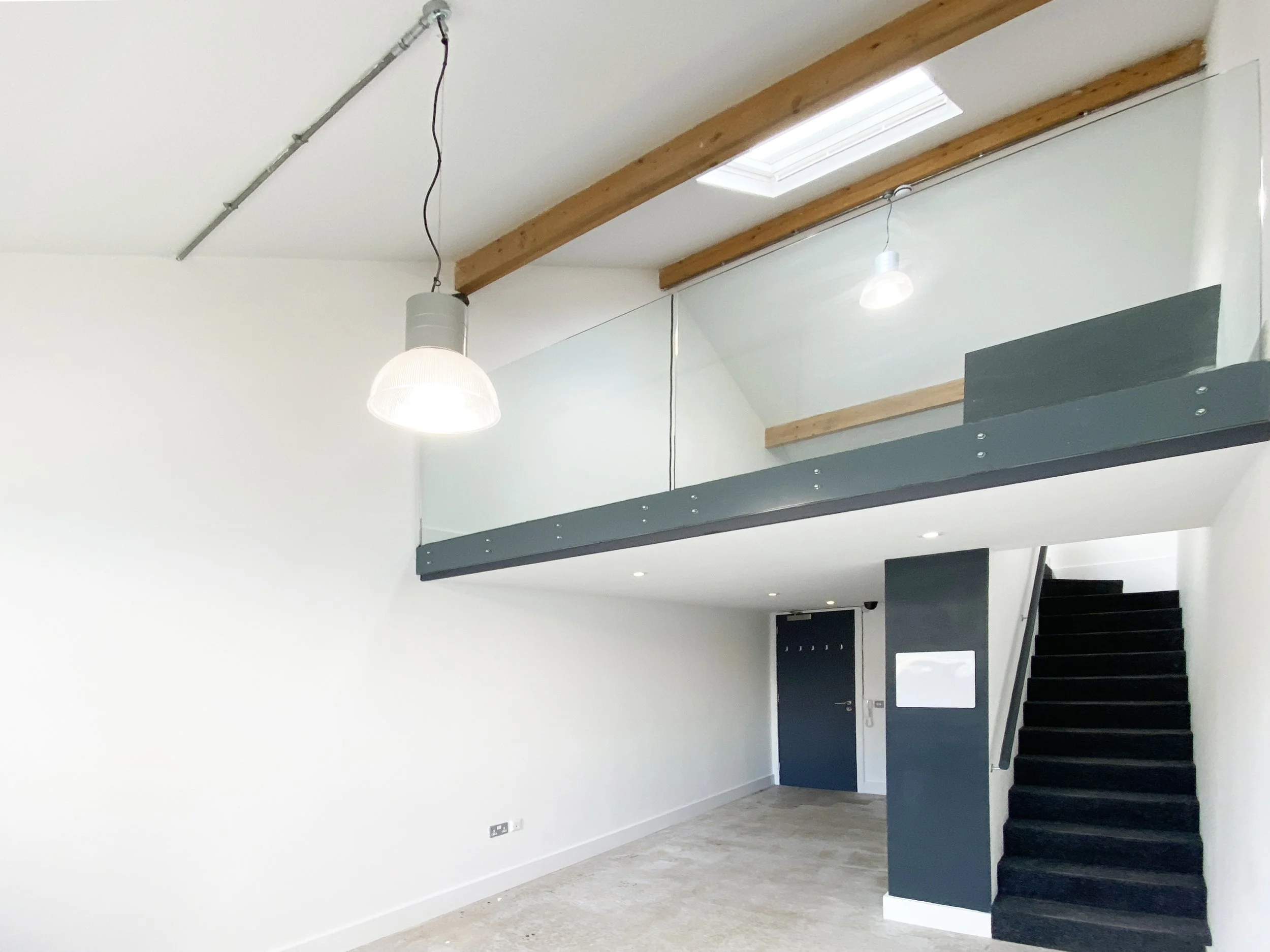 Studio Offices, Baltic Triangle Interior view of a modern home with staircase, large window, hanging lights, and wooden beams on the ceiling.
