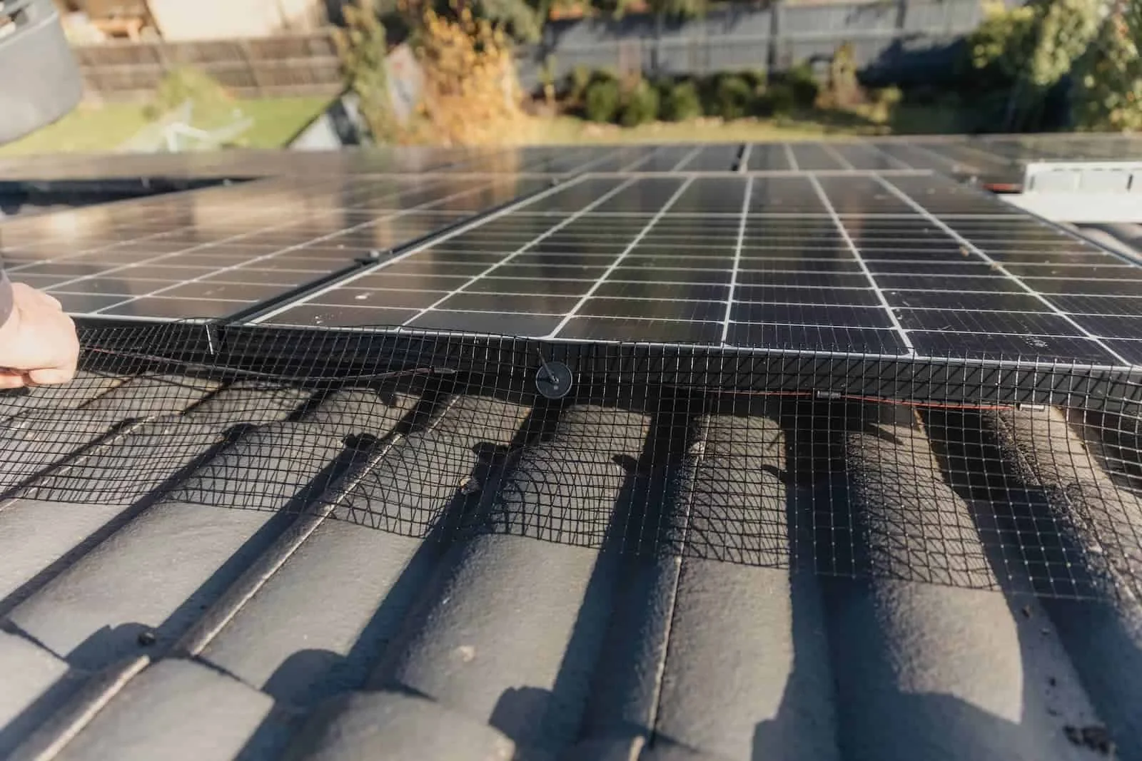 Black mesh critter guard mesh installed around solar panels on a red tile roof with J-hook clips to block birds and pests.