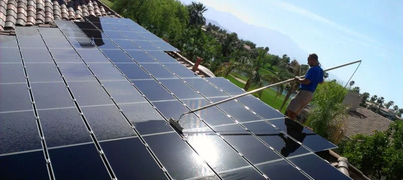 Technician in straw hat cleaning rooftop solar panels with pure-water soft-wash brush.