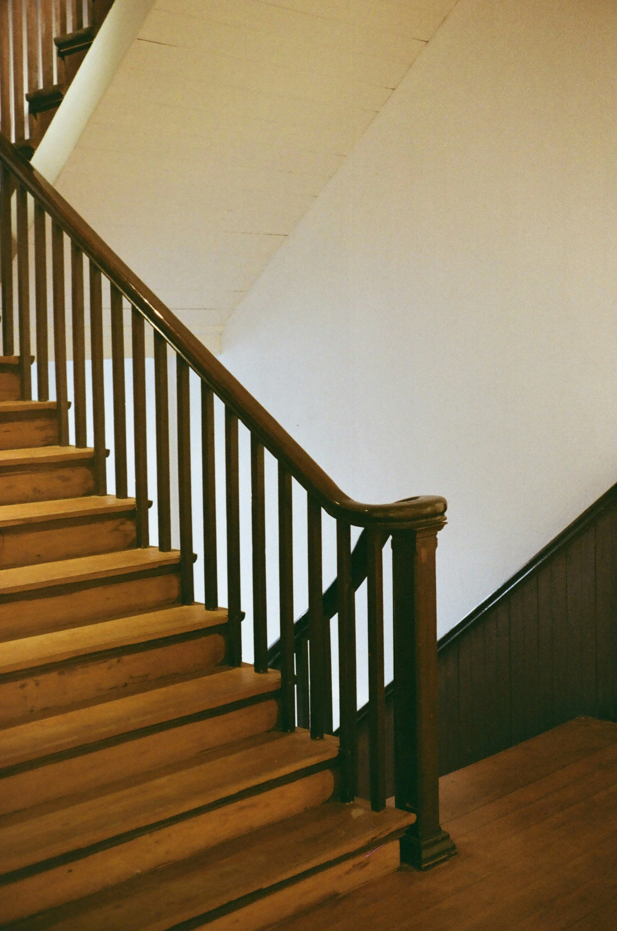 Escalier en bois avec rampe en bois foncé et barreaux noirs, montée vers un étage supérieur.