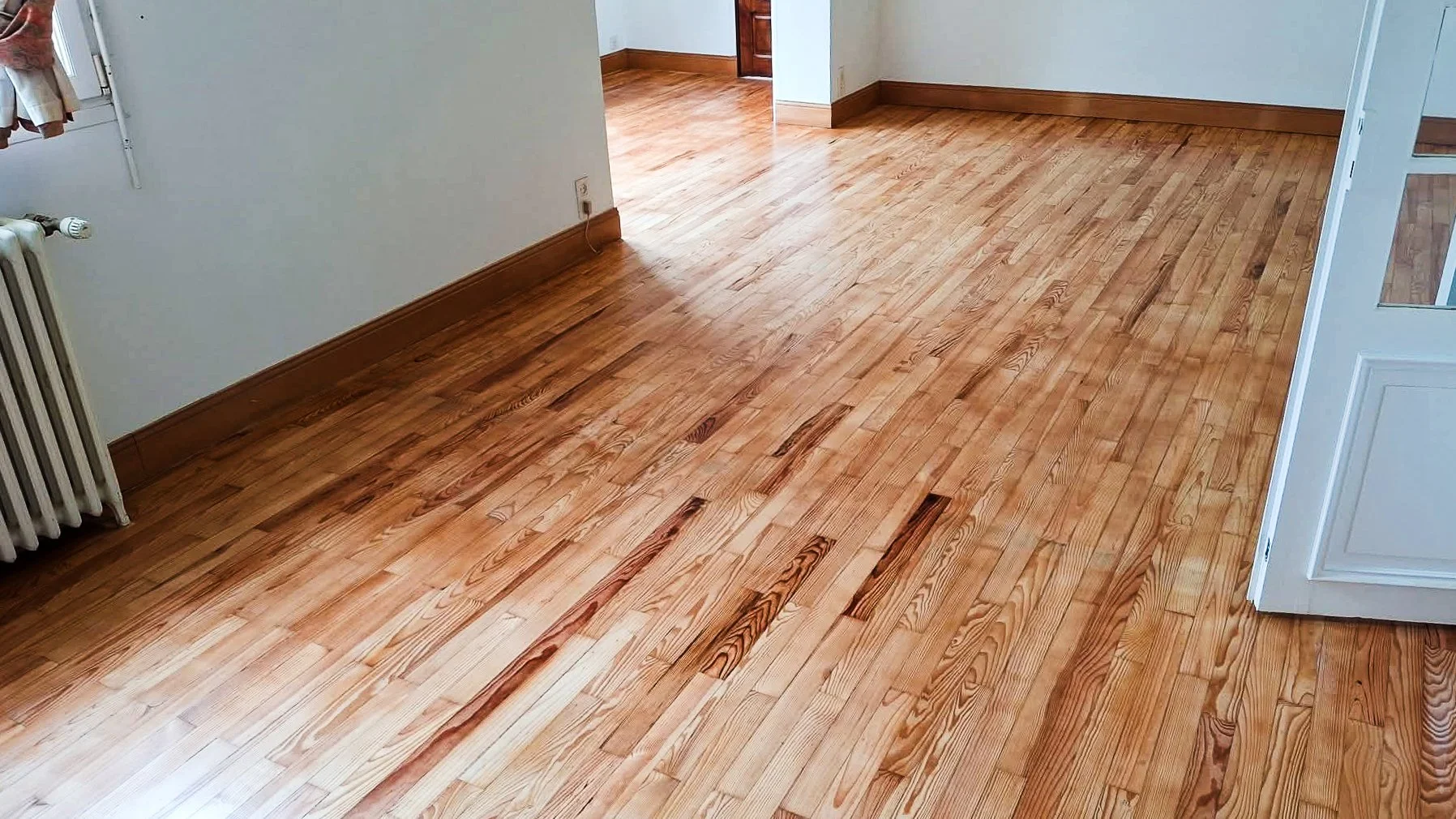 Plancher en bois dans une pièce intérieure, avec une porte et un radiateur visible.