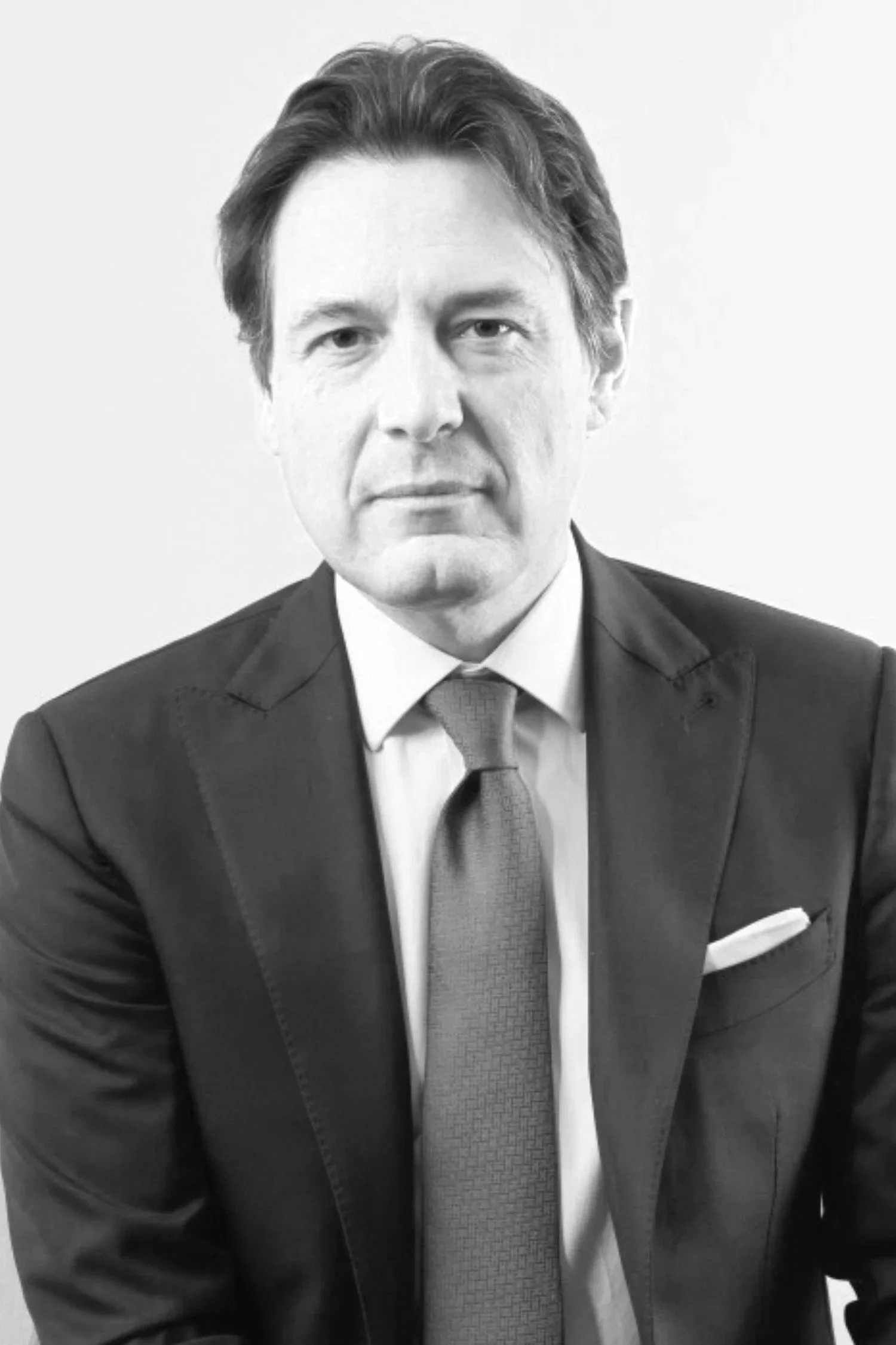 Black and white portrait of a man in a suit and tie, looking directly at the camera with a serious expression.