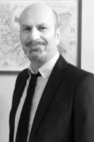 Black and white photo of a man with a bald head, beard, and mustache, wearing a suit and tie, smiling at the camera.