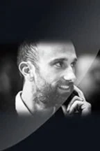 Black and white close-up of a man with a beard and short hair, smiling and looking to the side.