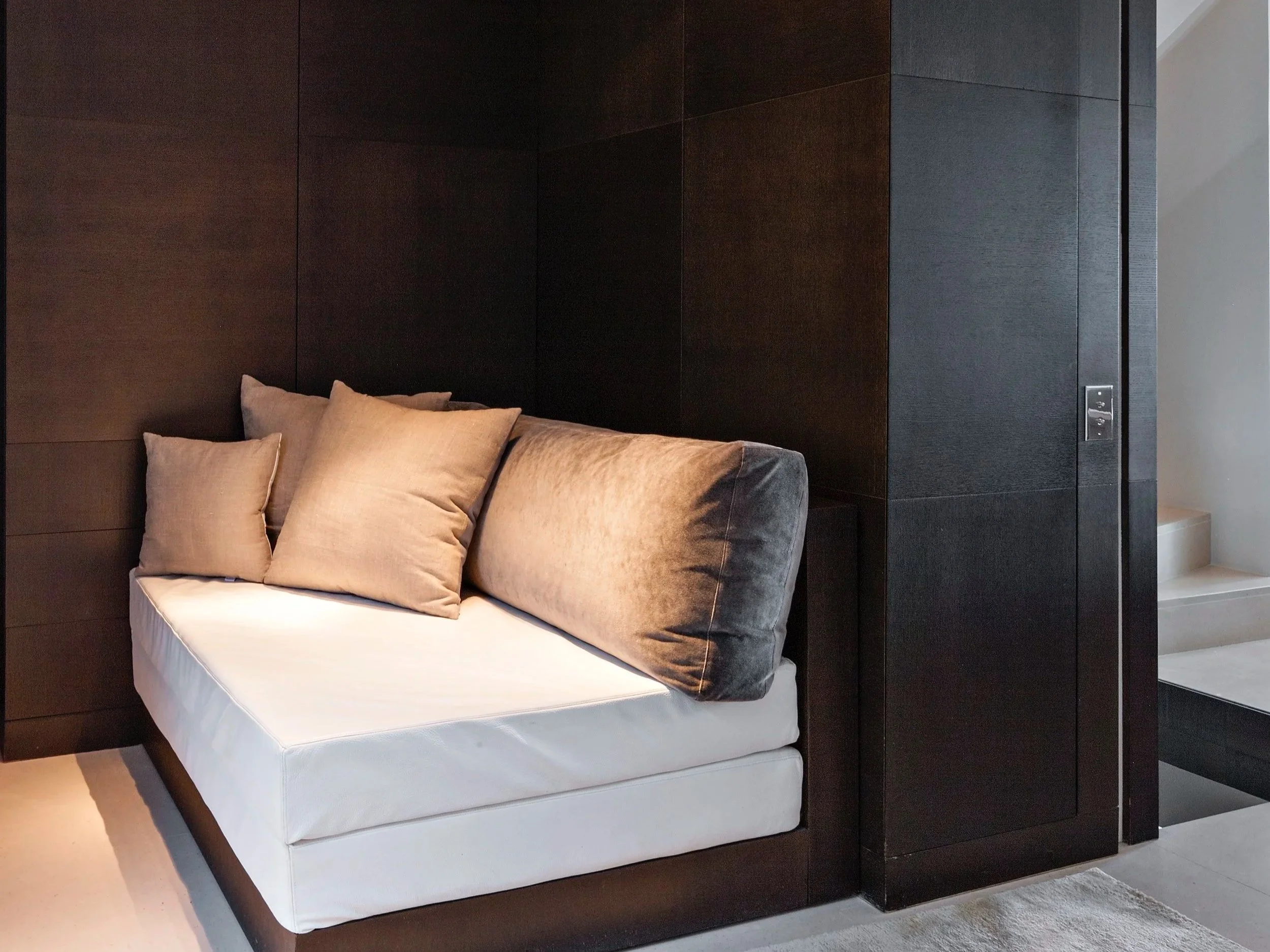 Canapé blanc avec plusieurs coussins beige dans une pièce avec murs en bois foncé et un mur blanc en arrière-plan