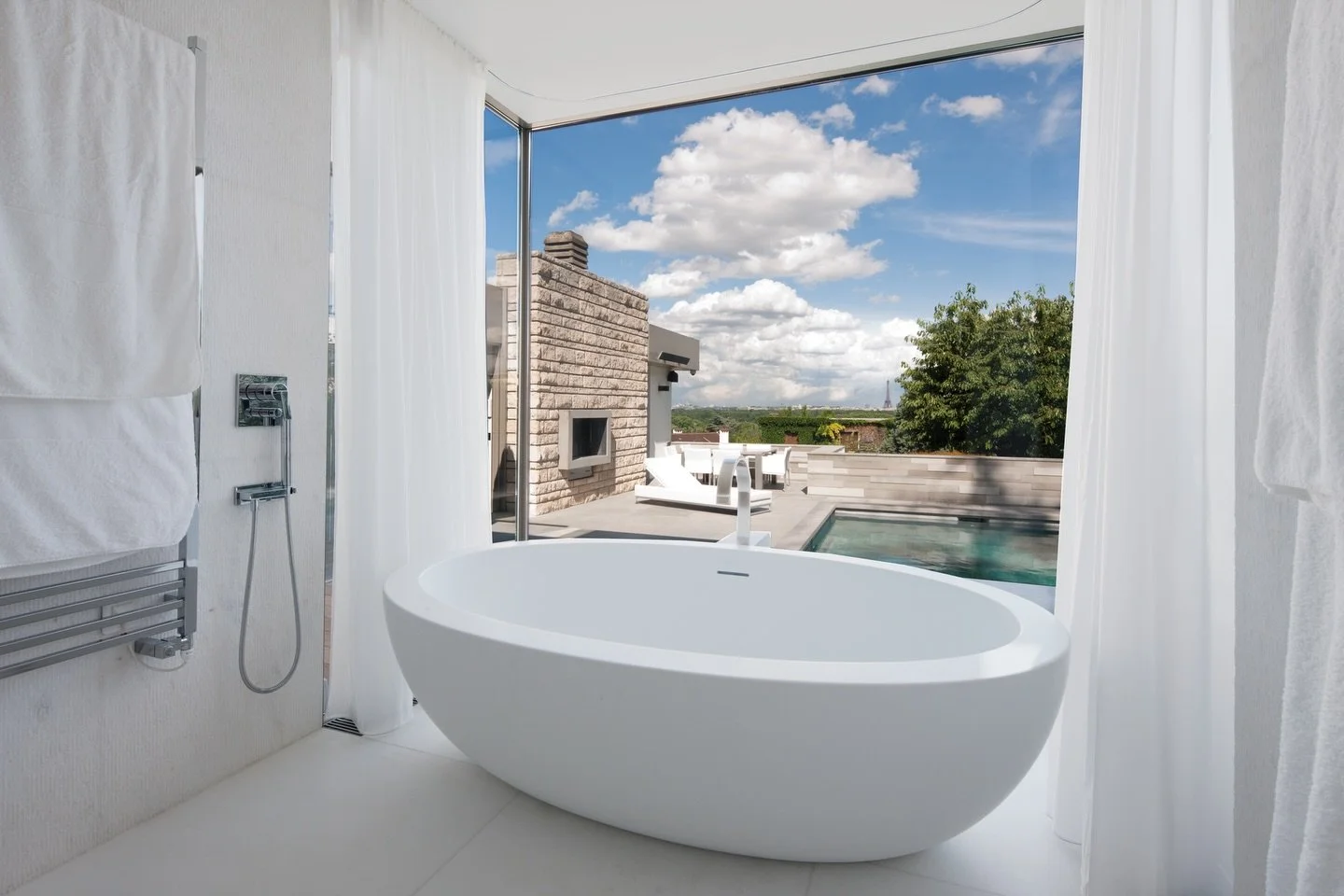 A sculptural bathtub overlooking Paris.
Framed by large openings, the space extends towards a panoramic view where the Eiffel Tower punctuates the horizon. Reflections and mineral textures create a calm and immersive atmosphere.

Styling &amp; Decora