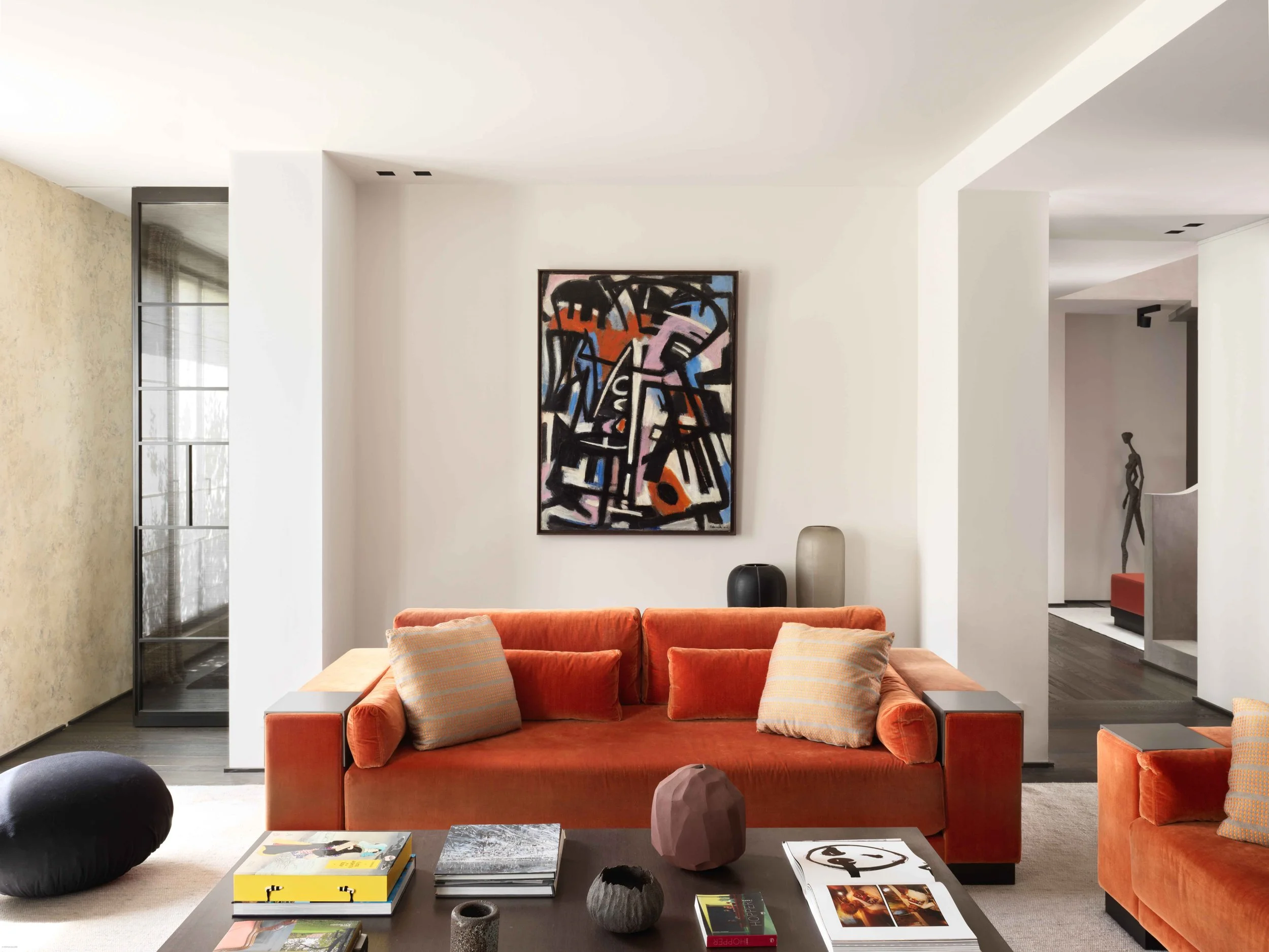 Salon moderne avec canapé orange, tableaux, objets décoratifs, et sculpture au fond.