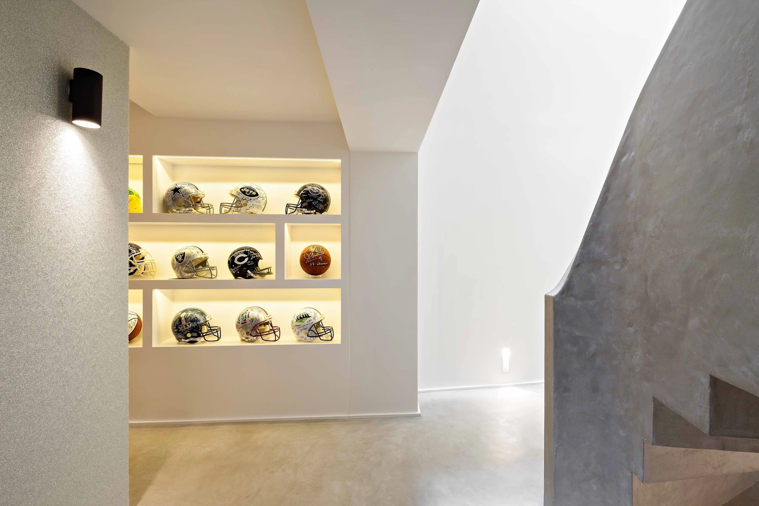 Vitrine avec plusieurs casques de football américains et un ballon dans un intérieur moderne.