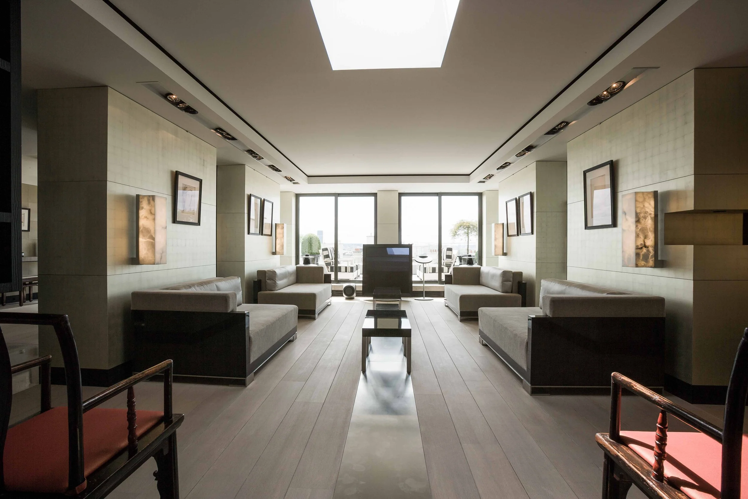 Salle de séjour moderne avec canapés beige et œuvres d'art sur les murs, grandes fenêtres avec vue sur l'extérieur, sol en bois clair, éclairage encastré au plafond.