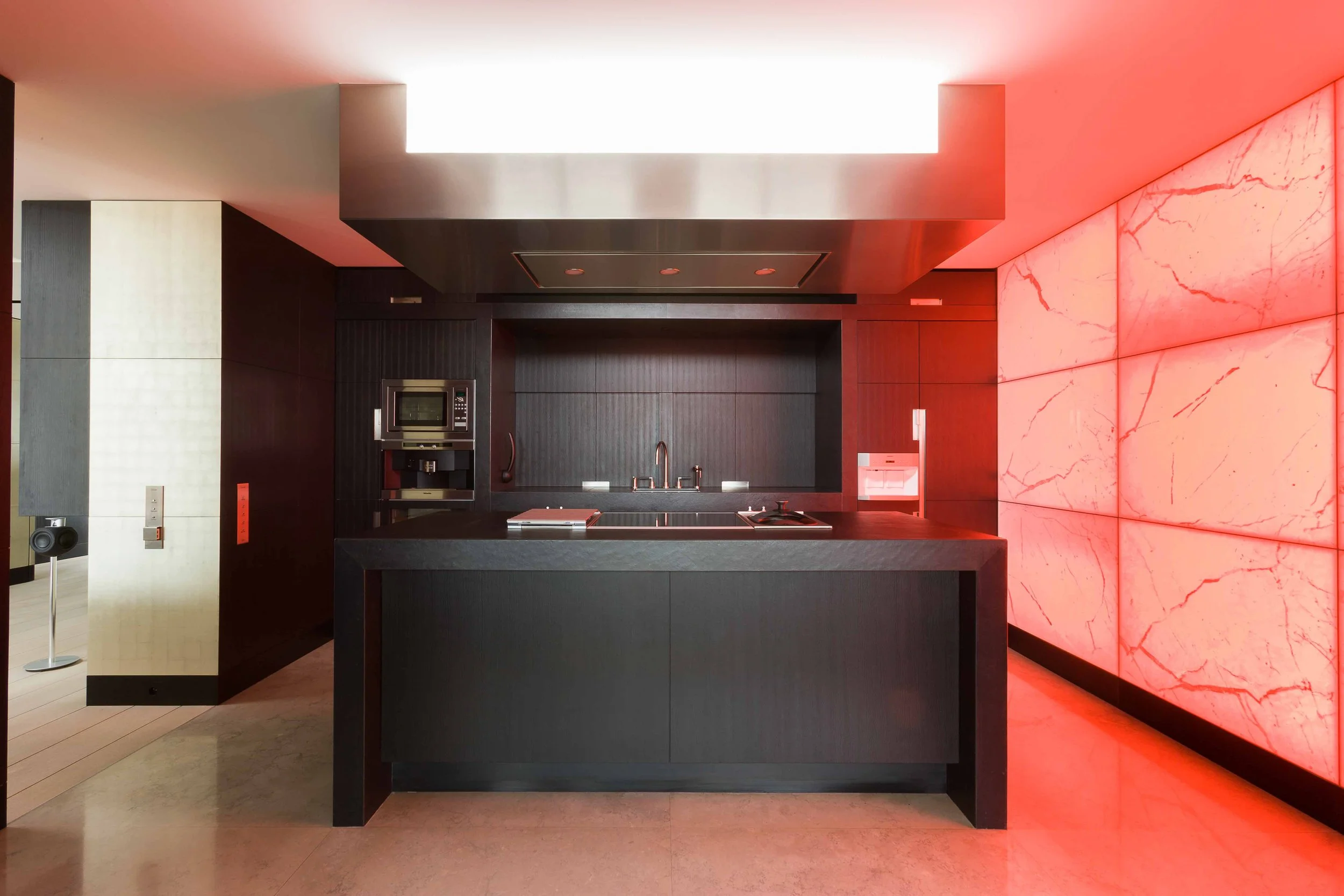 Cuisine moderne avec un îlot noir, murs noirs, une paroi en marbre rose, appareils électroménagers intégrés et éclairage tamisé