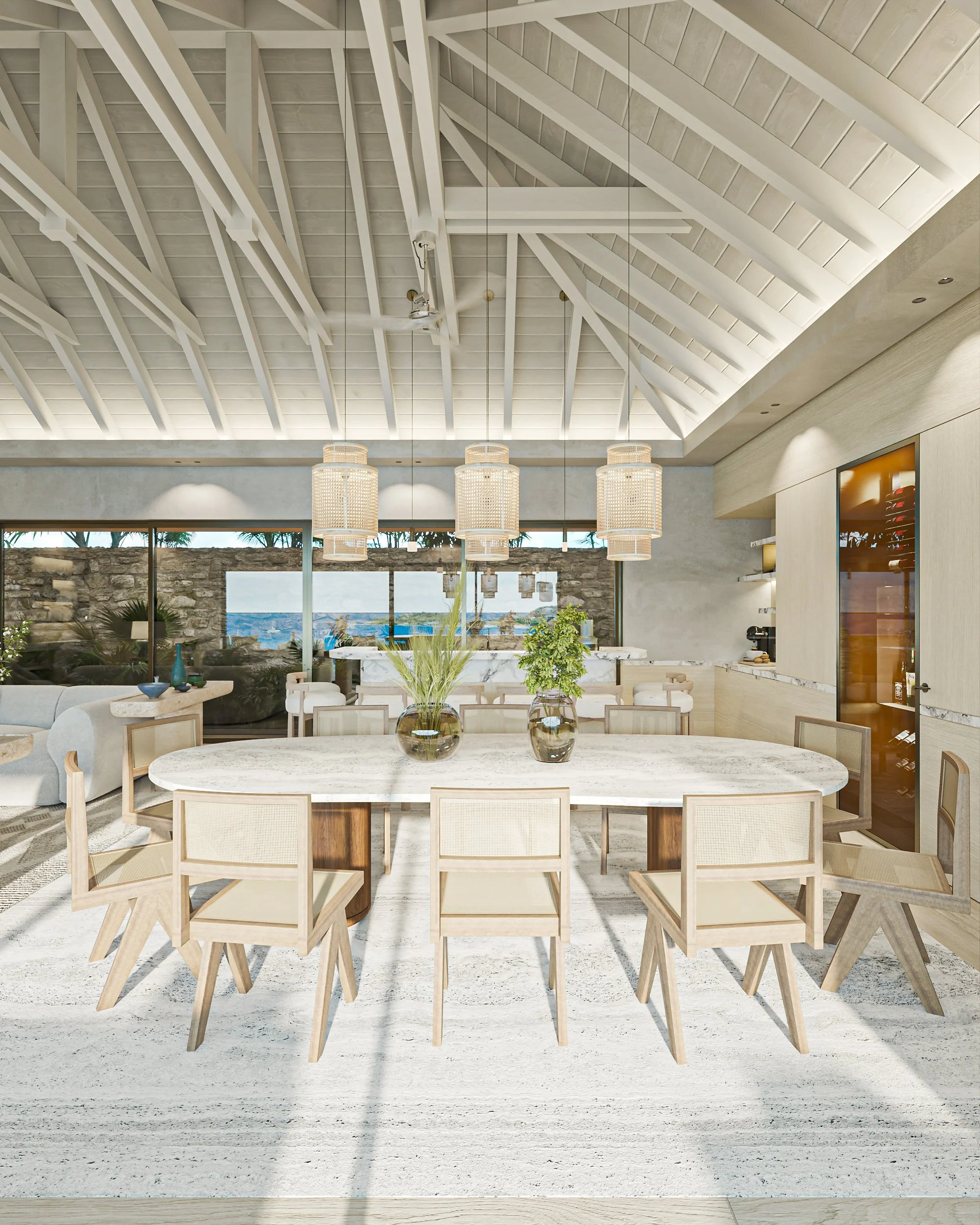 Intérieur d'une salle à manger lumineuse avec un plafond en pente en bois blanc, un grand tapis blanc, une table ovale en marbre entourée de chaises en bois clair, et des vases avec des plantes au centre de la table. En arrière-plan, une baie vitrée 