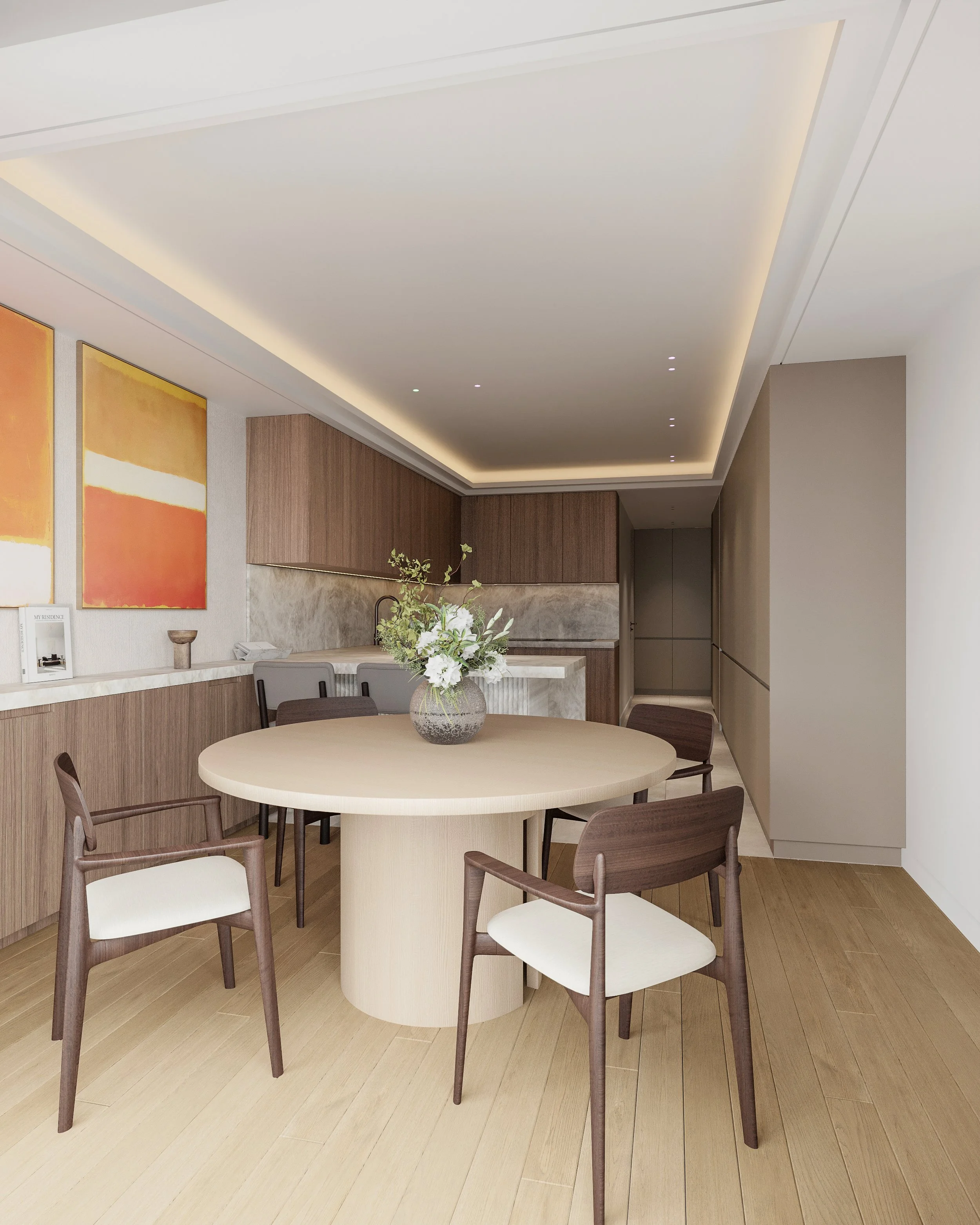 Salle à manger minimaliste avec un table ronde en bois clair, quatre chaises en bois foncé avec assises blanches, une vase avec des fleurs sur la table, une cuisine en arrière-plan avec des meubles en bois et un plan de travail en marbre, et un plafo