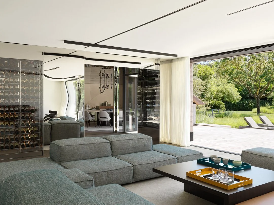 Salons modernes avec canapé gris, table basse noire, vue sur jardin extérieur avec chaises longues et grand arbre