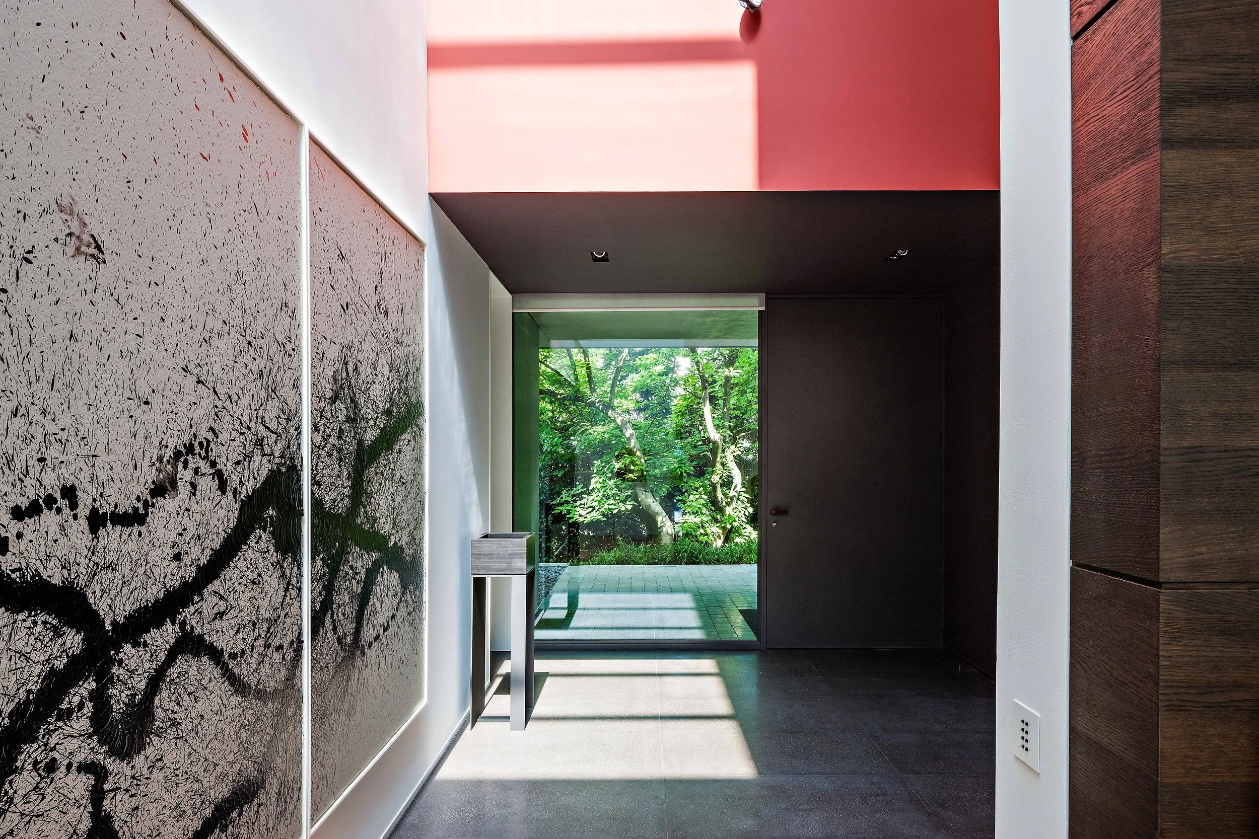 Intérieur moderne avec mur d'art abstrait, porte noire, vue sur un jardin avec des arbres à travers une grande fenêtre.