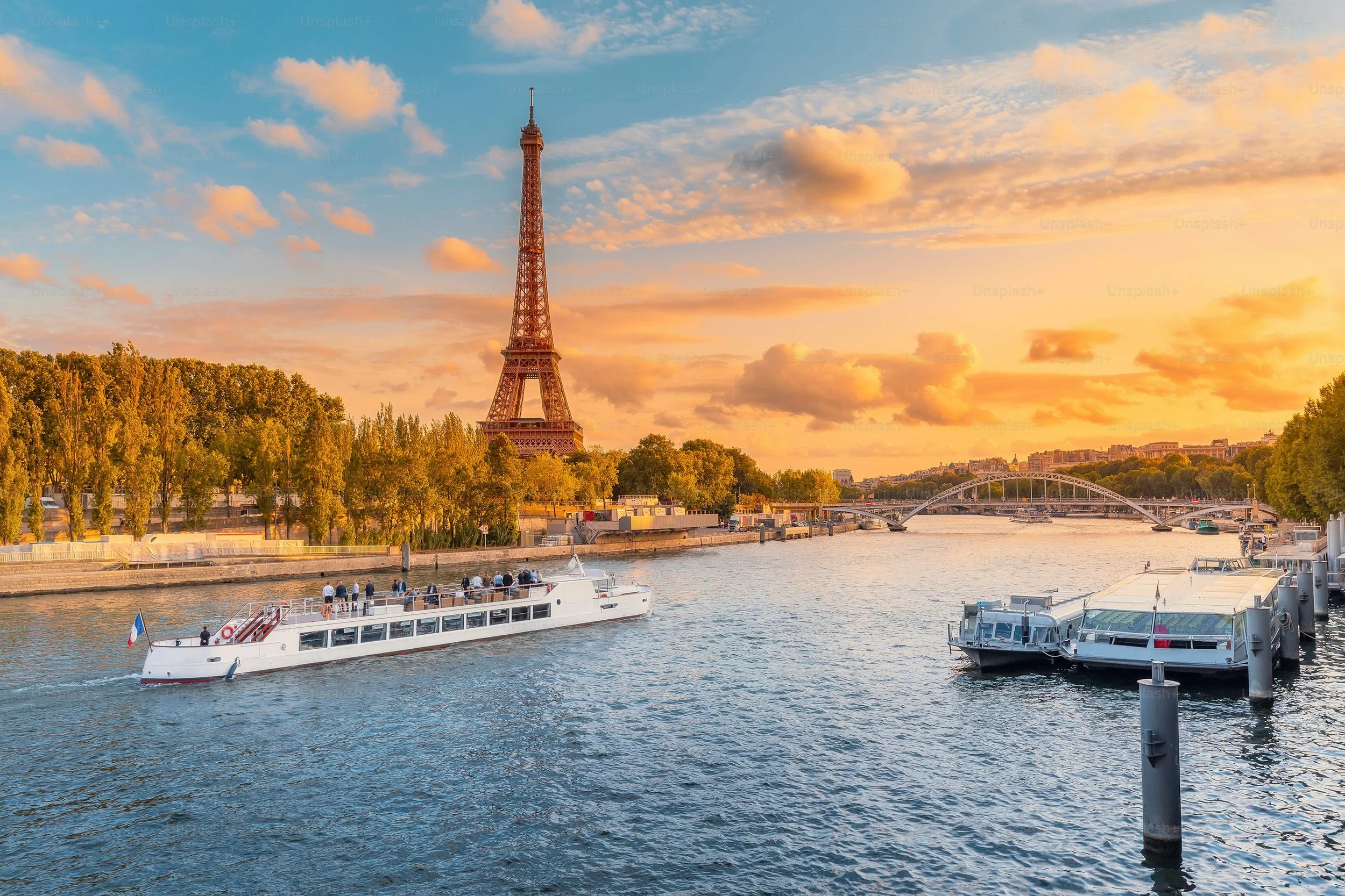 Vue du fleuve Seine à Paris avec la Tour Eiffel au coucher du soleil, bateaux sur l'eau, et arbre le long de la rive.