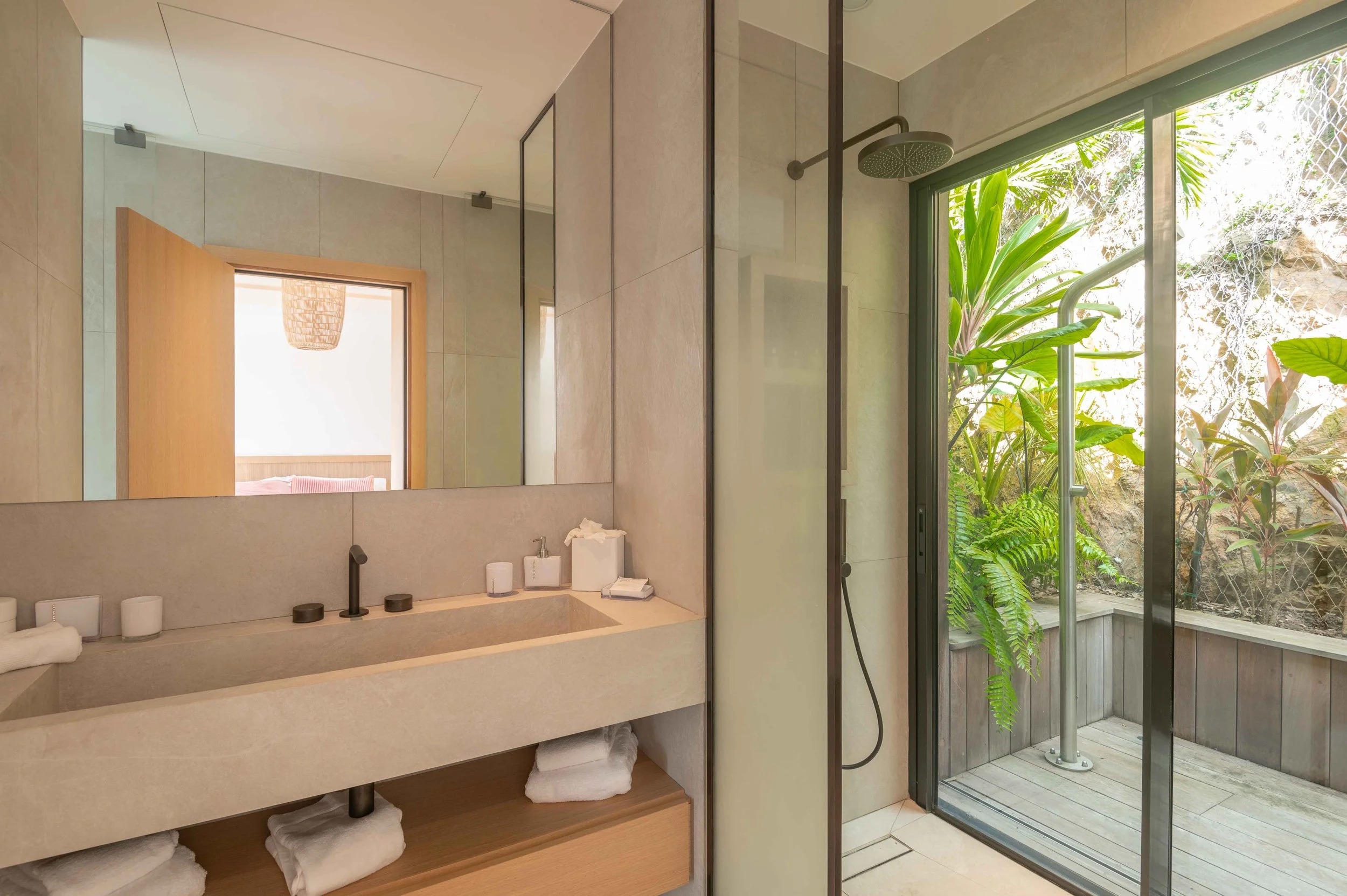 Salle de bain moderne avec lavabo en pierre, miroir, douche extérieure avec vue sur un jardin tropical
