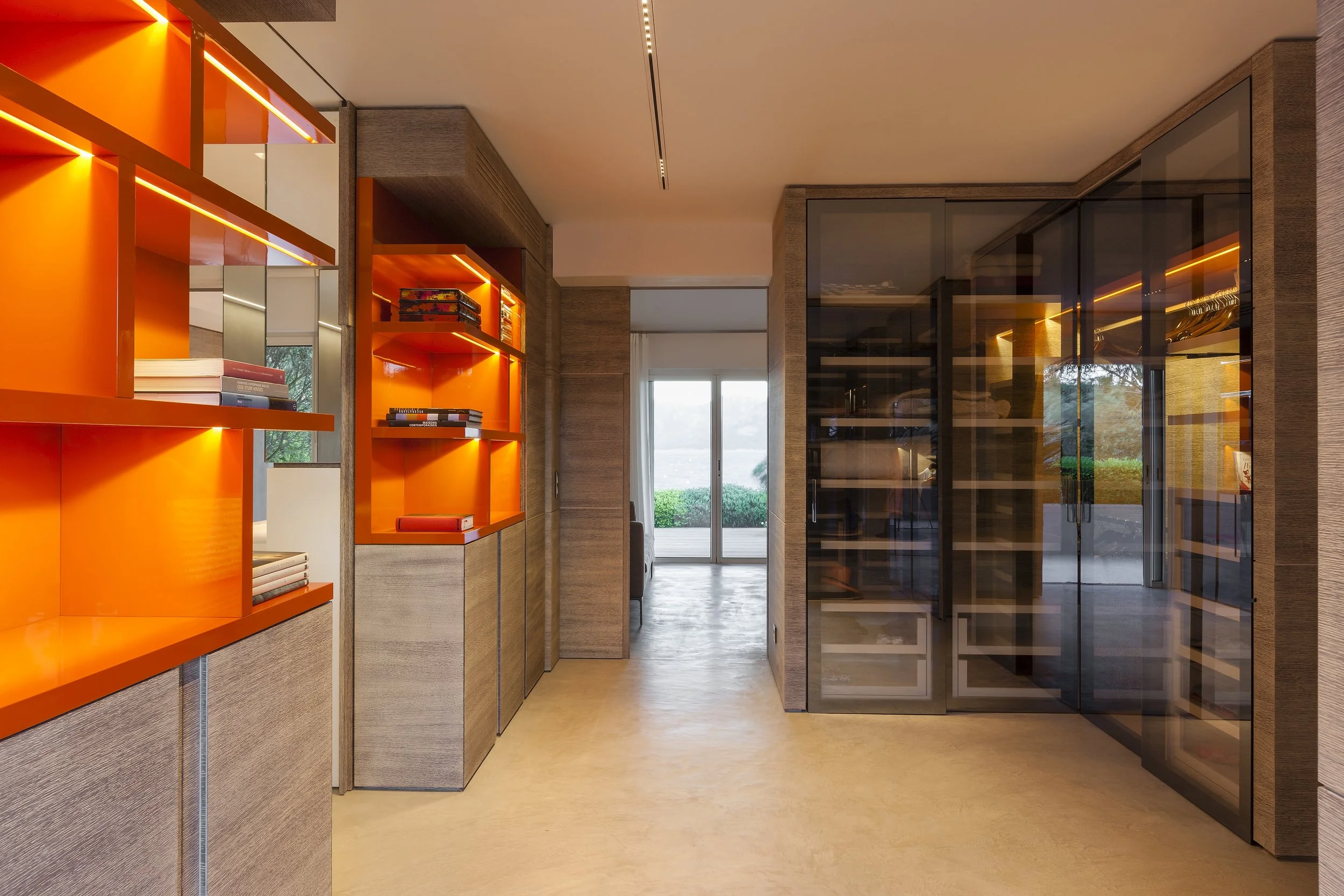 Intérieur d'une pièce moderne avec des étagères oranges, un placard en verre noir, et une vue sur un patio extérieur par une porte-fenêtre.