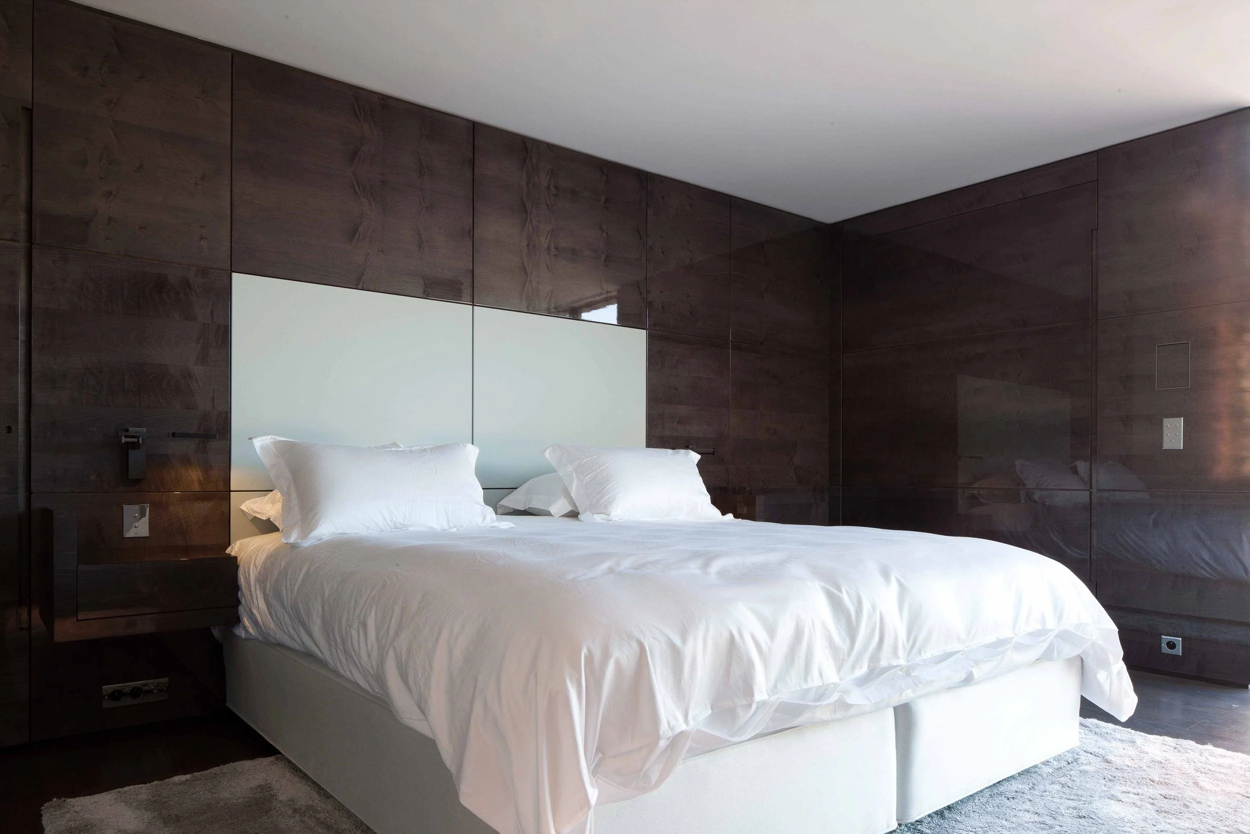 Chambre moderne avec lit à lits jumeaux, draps blancs, murs en bois foncé et tête de lit blanche