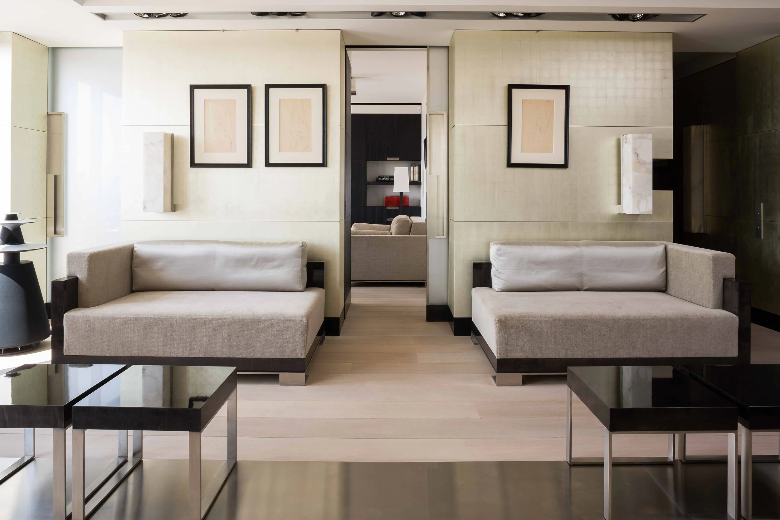 Salon moderne avec deux canapés beiges, tableaux noir et blanc sur la paroi, tables basses en métal noir avec dessus en miroir, décoration minimaliste, lumière naturelle