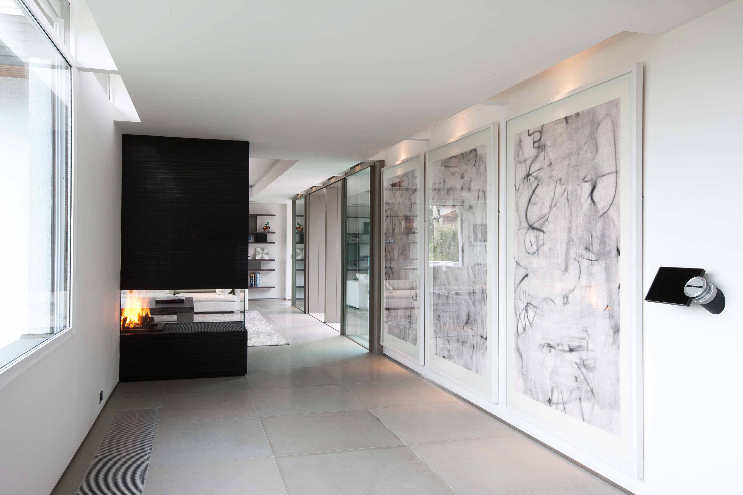 Intérieur moderne avec un mur blanc, un poêle à bois noir, des œuvres d'art abstrait en noir et blanc sur un mur, et des étagères avec des livres