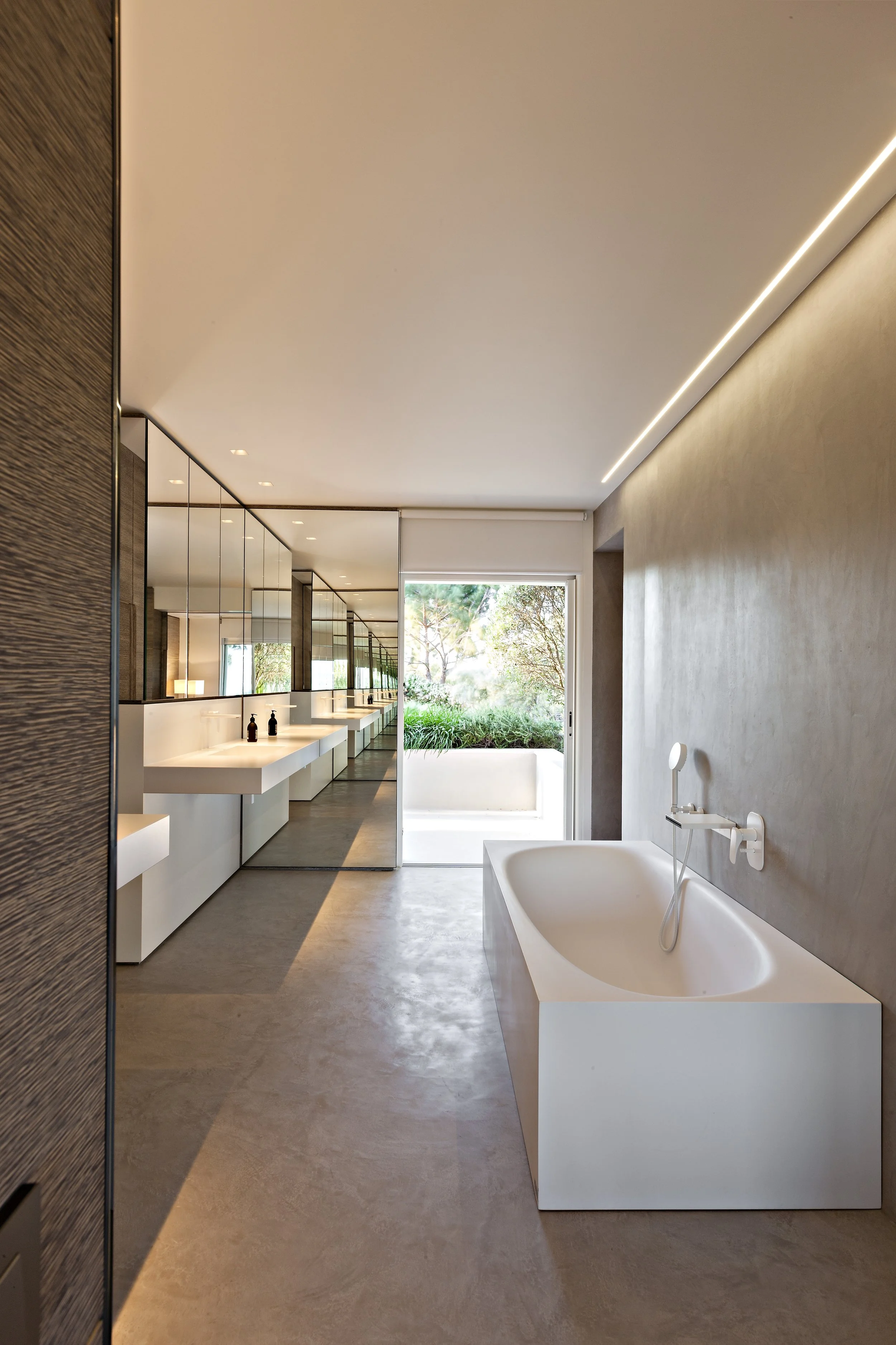 Salle de bain moderne avec une grande baignoire blanche, un mur en béton, et un lavabo avec un miroir et une lumière LED